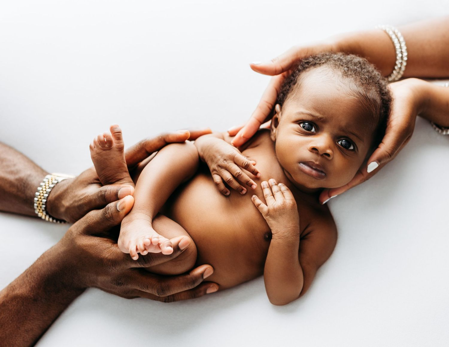 Gentle hands with bracelets cradle and support a small baby lying on a white background.
Rashinphotography-Nova photographer- DMV DC