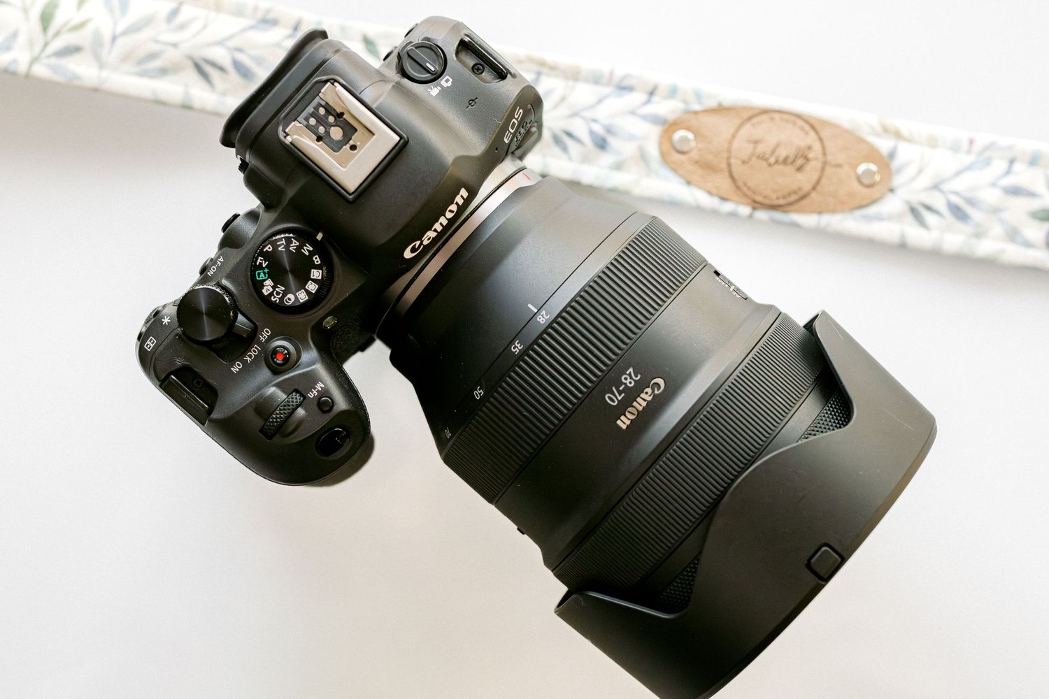 Canon camera with decorative floral camera strap on denim surface.