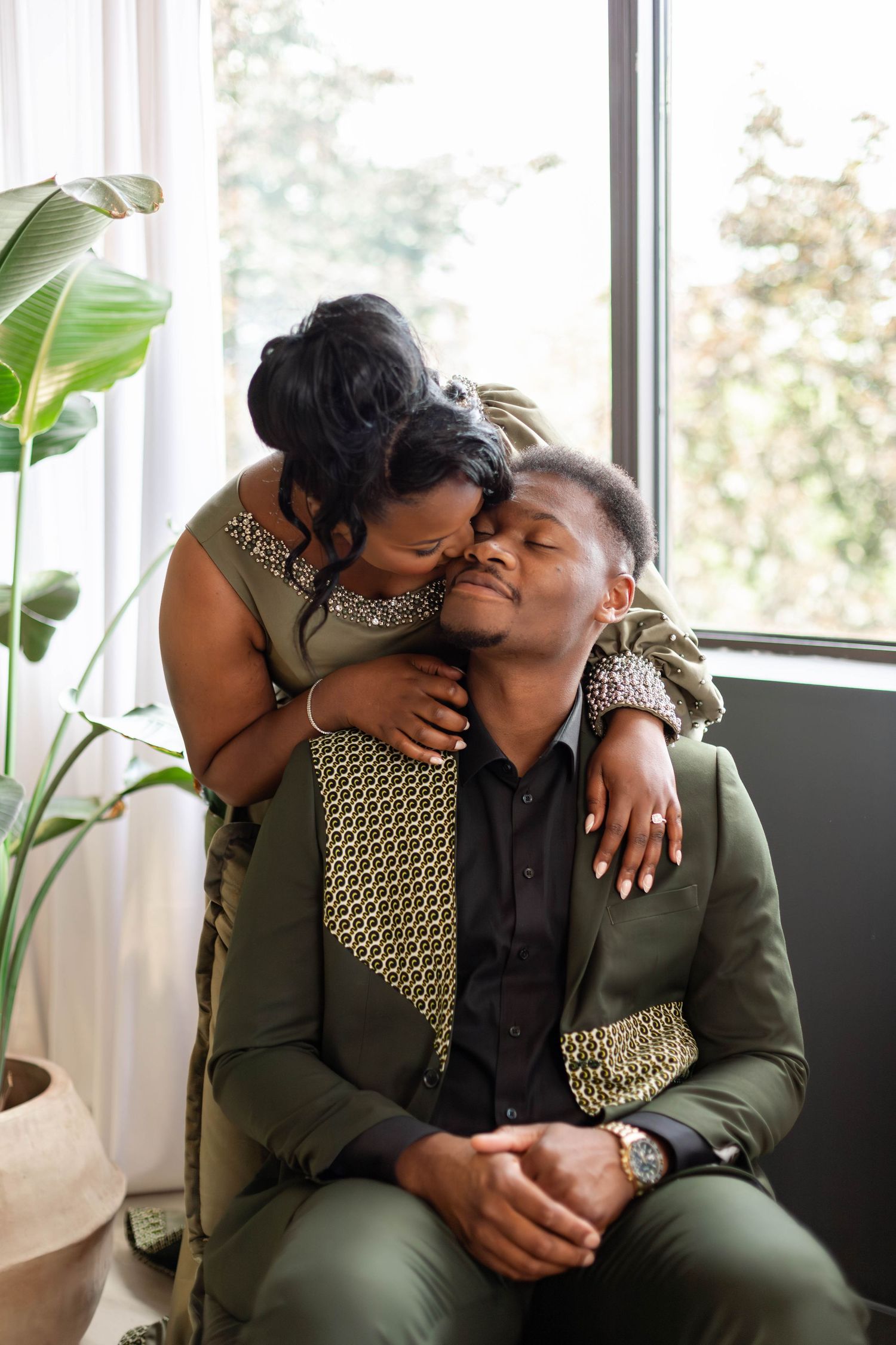 An intimate moment between a couple in coordinating olive green outfits near a window.