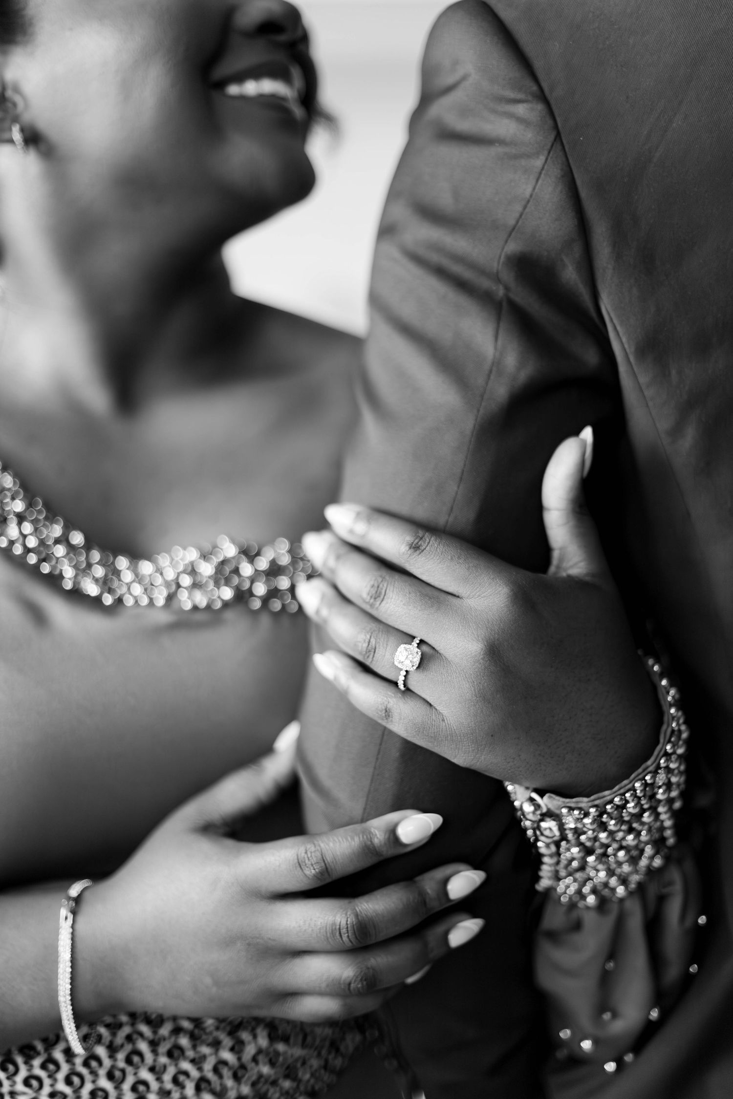 Black and white close-up of hands wearing jewelry and embracing in formal attire.