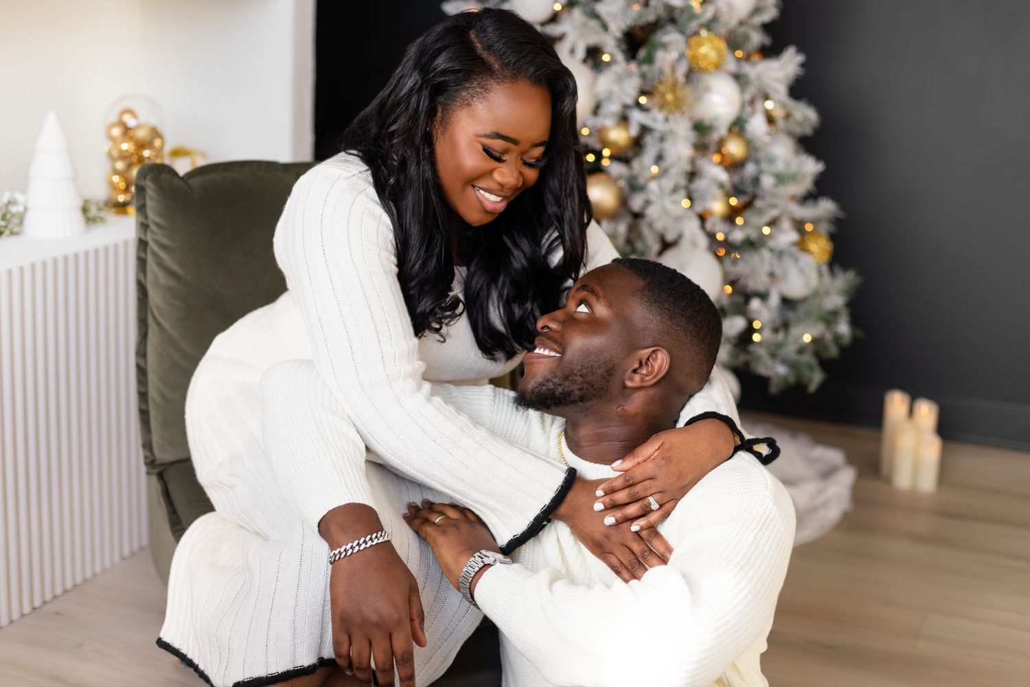 Couple in white outfits sharing joyful moment by decorated Christmas tree.