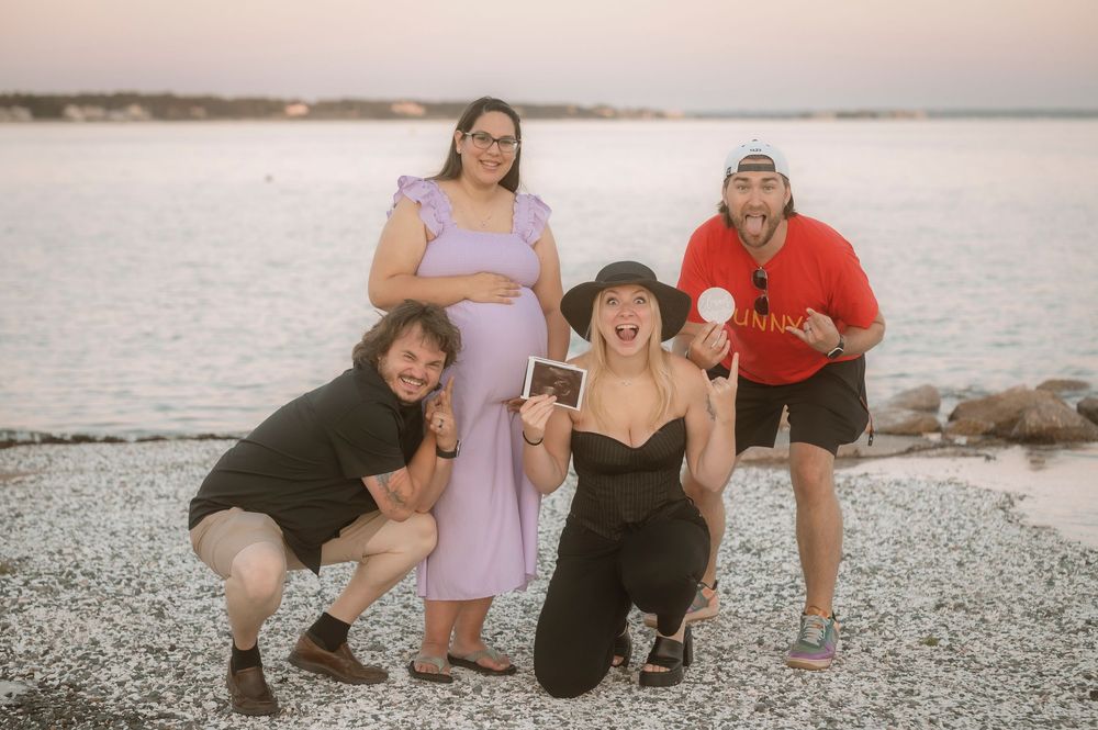Group of friends laughing and posing together on a rocky beach at sunset with water in the background.