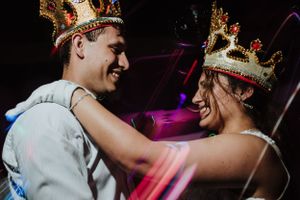 Newlywed couple wearing decorative crowns smiling at each other during festive wedding reception. Fotógrafo de Bodas en Formosa