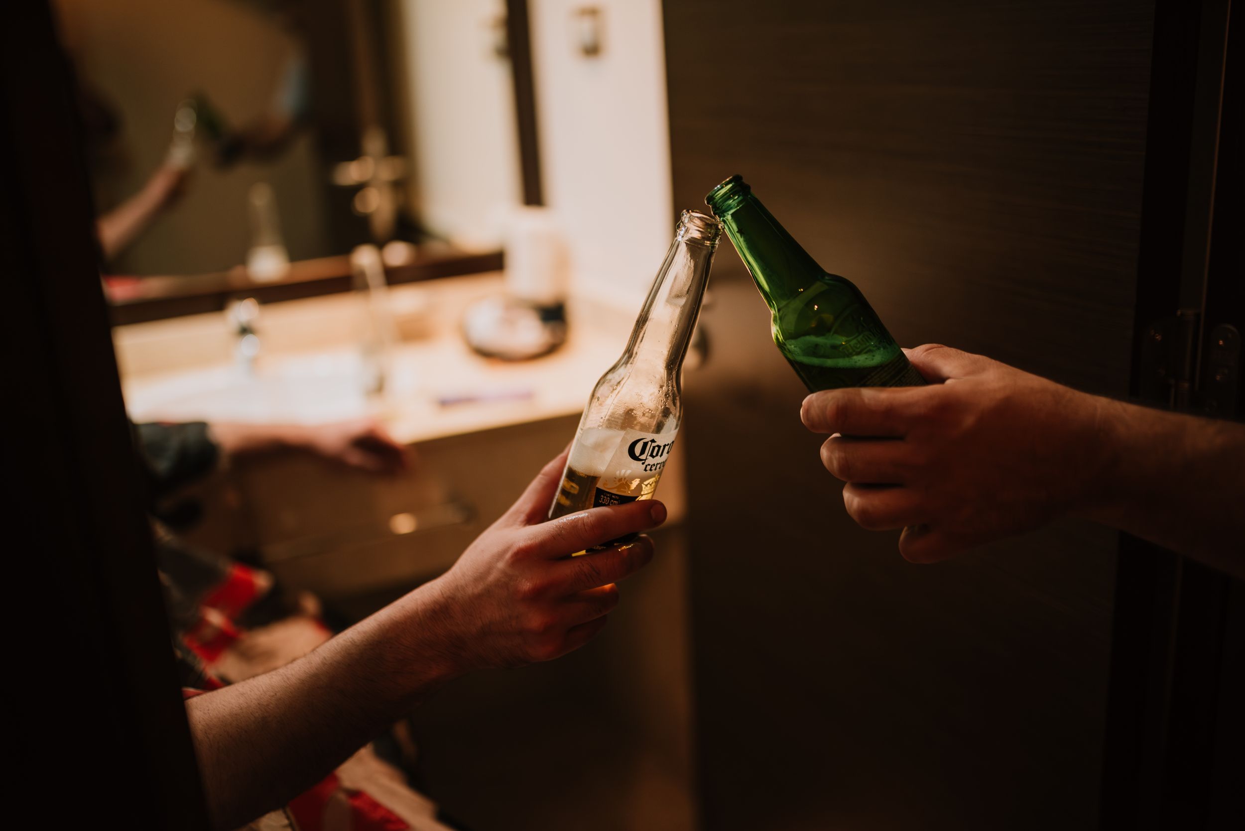 Two people clinking Corona beer bottles together in a warmly lit room. Fotógrafo de Bodas en Formosa