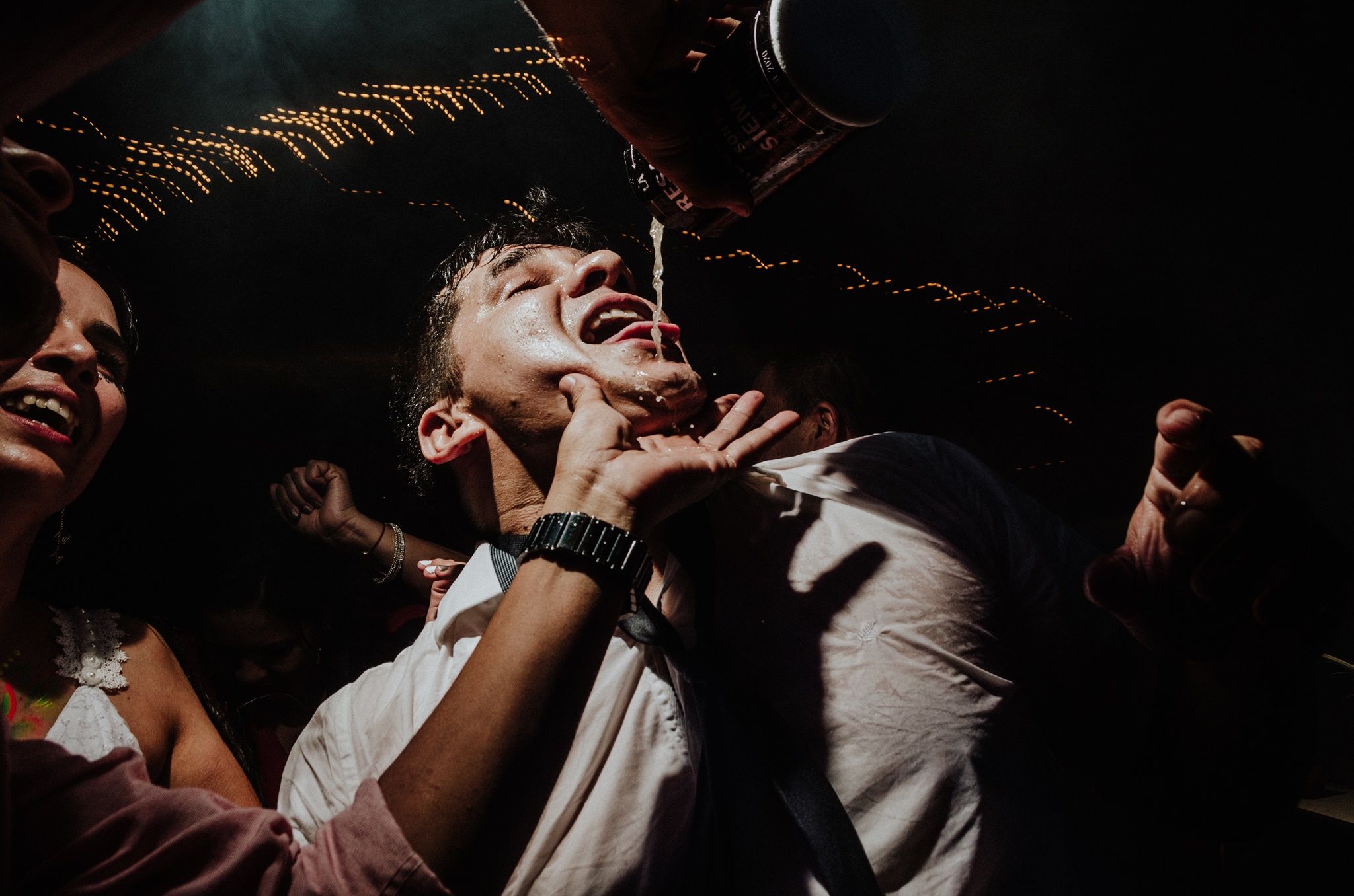 Young man laughing joyfully surrounded by friends at a dark festive party celebration. Fotógrafo de Bodas en Formosa