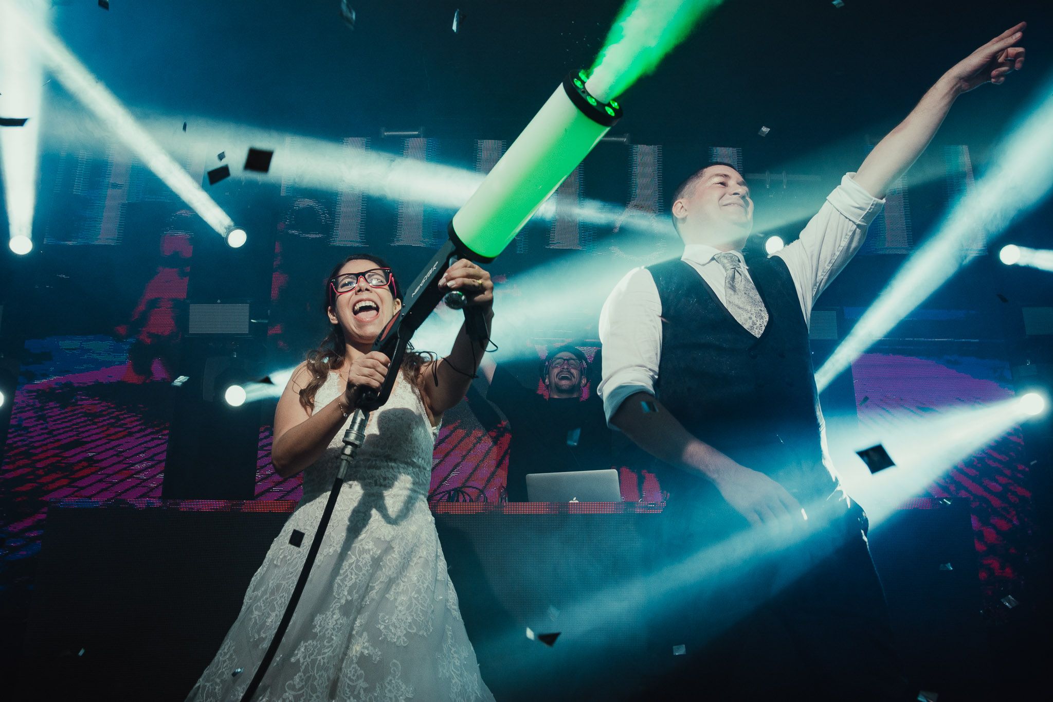 Bride and groom celebrate on a stage with green foam stick, confetti, and dramatic concert lighting. Fotógrafo de Bodas en Formosa