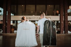 Bride and groom walking hand in hand carrying garment bags at outdoor wedding venue. Fotógrafo de Bodas en Formosa