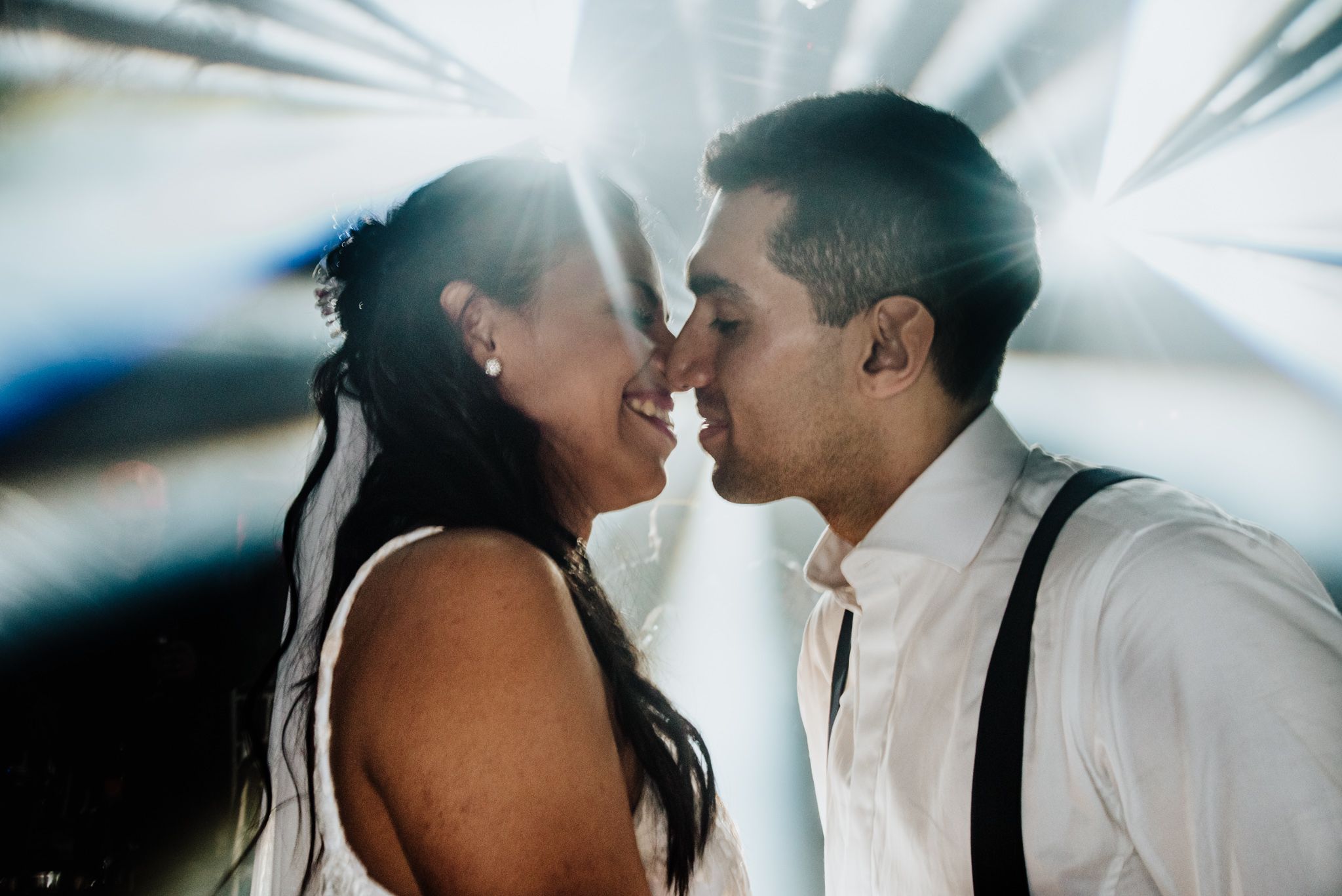 Bride and groom sharing romantic moment nose to nose with sunburst light effect behind them.