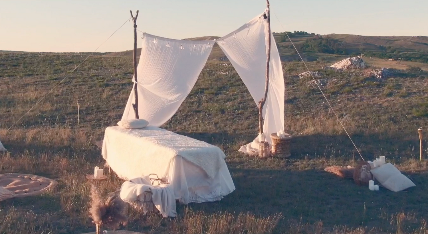White canopy bed setup outdoors in a rustic landscape during sunset.