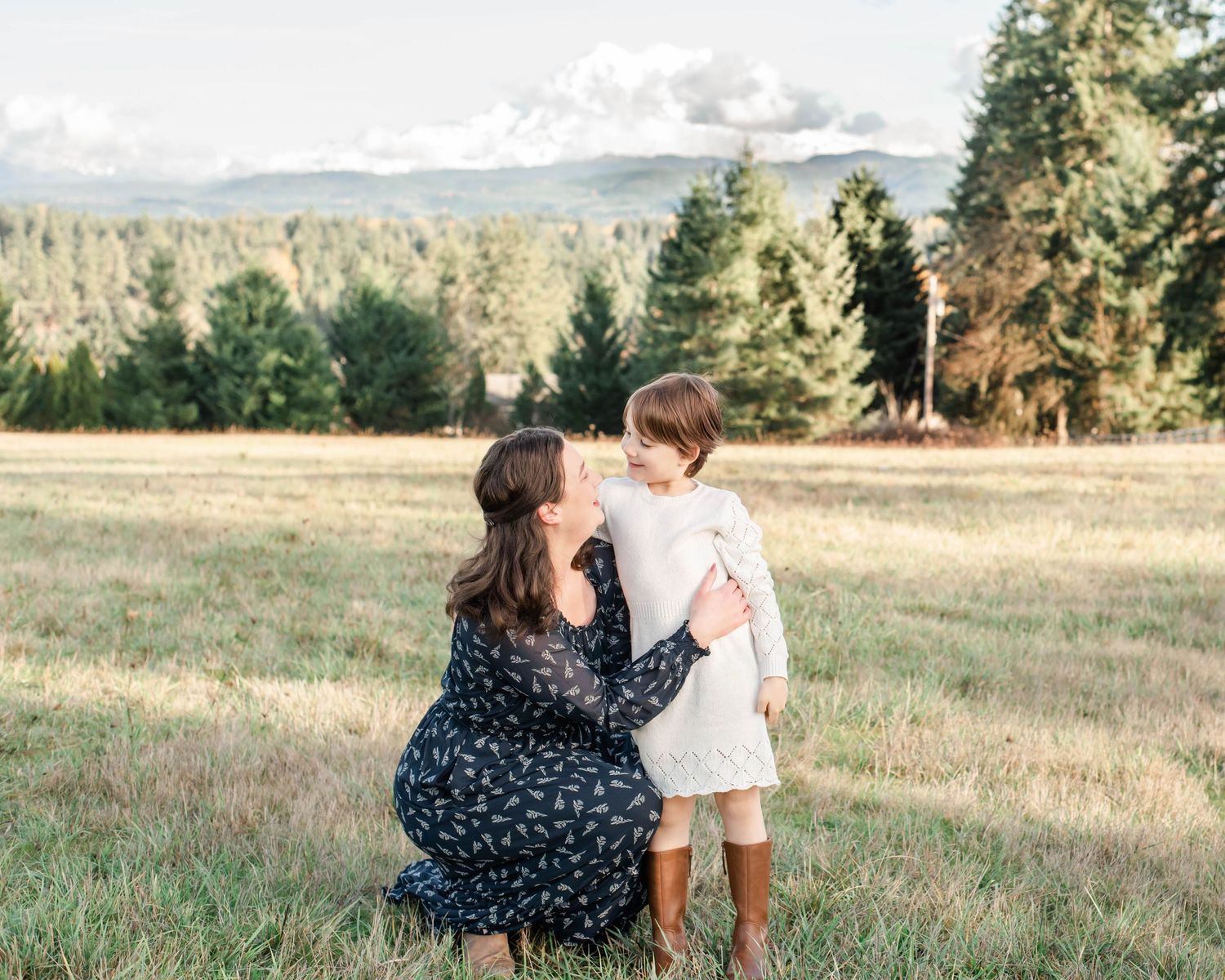 Mother and child sitting together in grassy field with mountain backdrop.