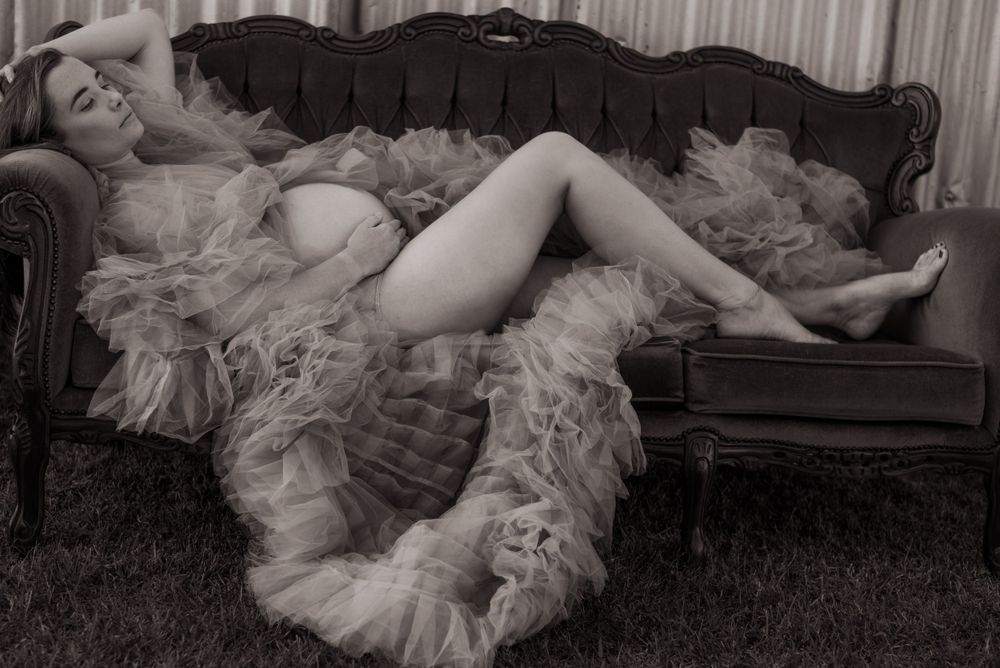 Vintage-style boudoir photo of figure reclining on antique couch with tulle fabric.