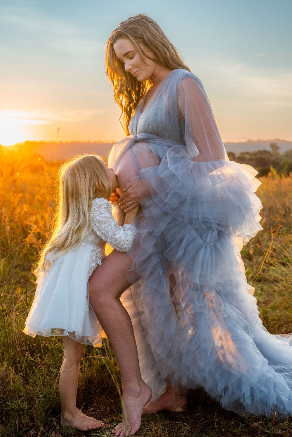 A touching maternity scene at sunset with a flowing gray dress in a golden field.