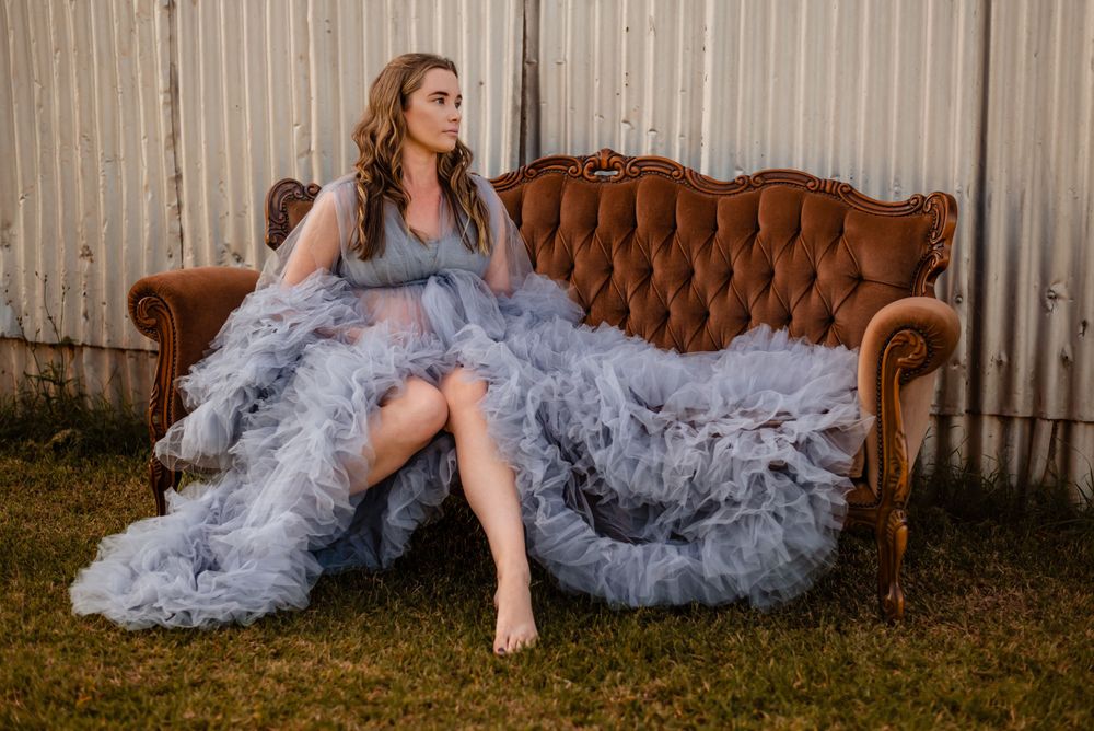 A maternity photo on a vintage brown couch features a flowing gray tulle dress.