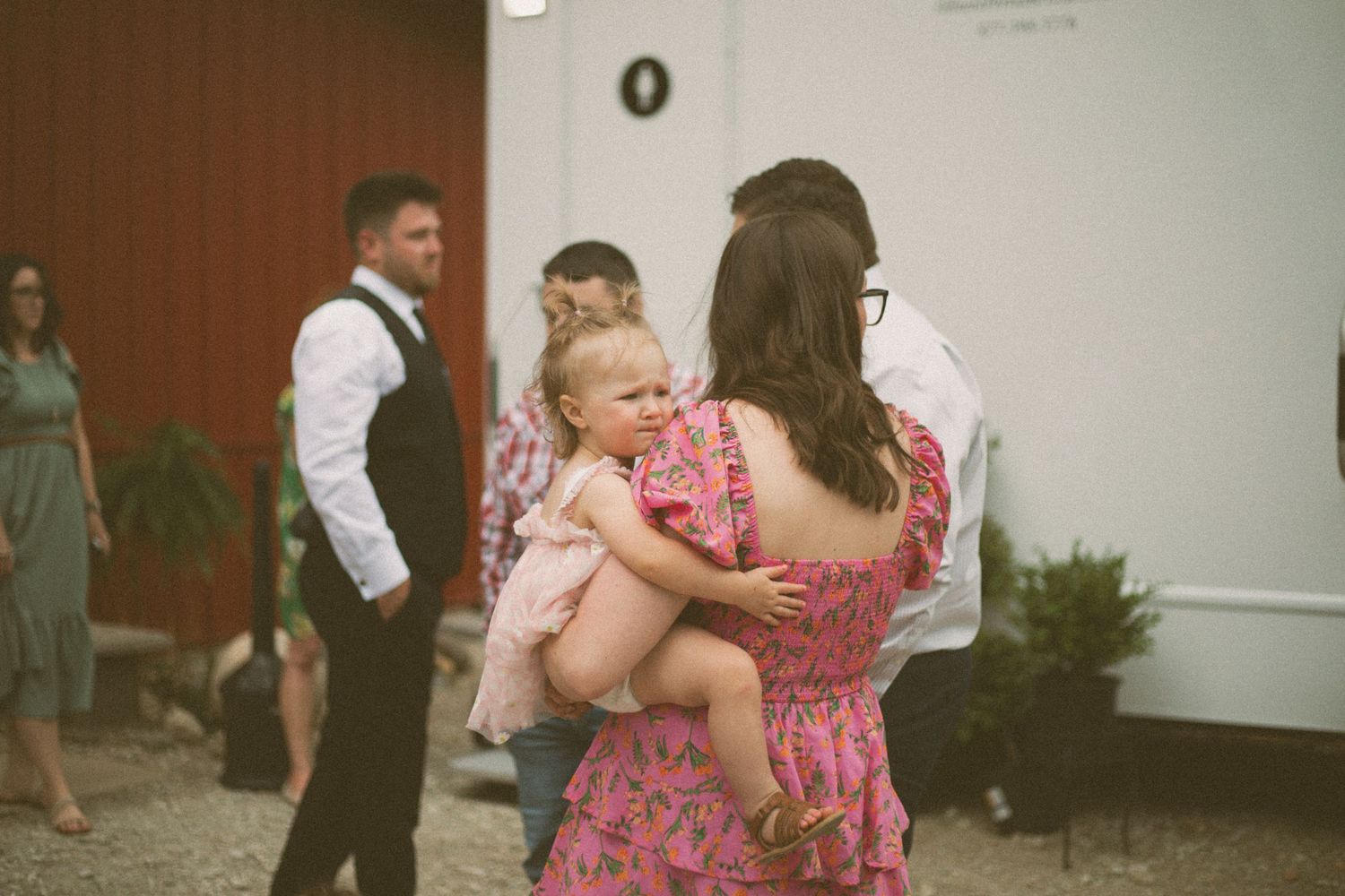 Woman in pink floral dress holds a small child during a casual outdoor gathering.