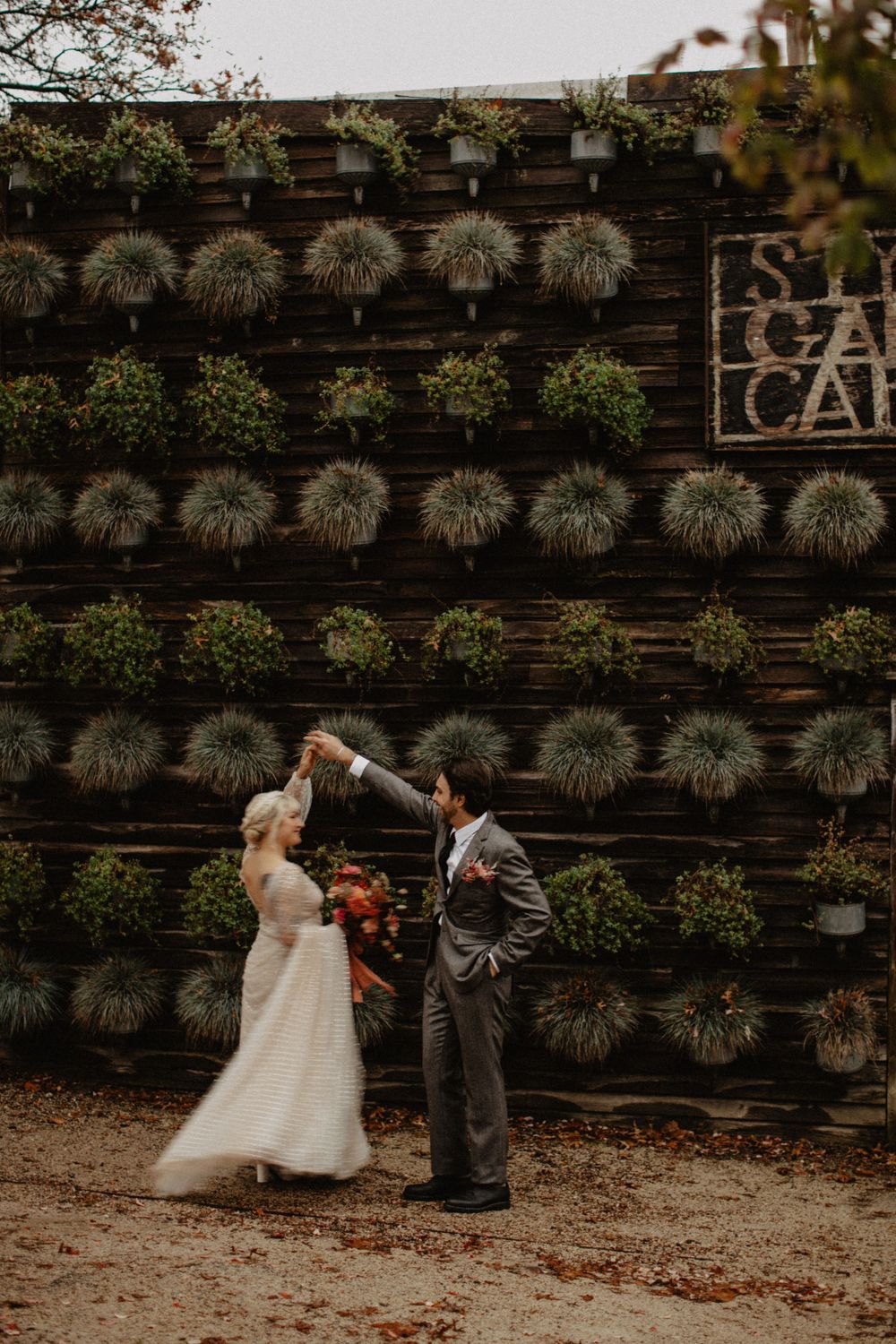 A couple shares a romantic moment in front of a living wall covered with ornamental grasses and plants at Terrain at Styers