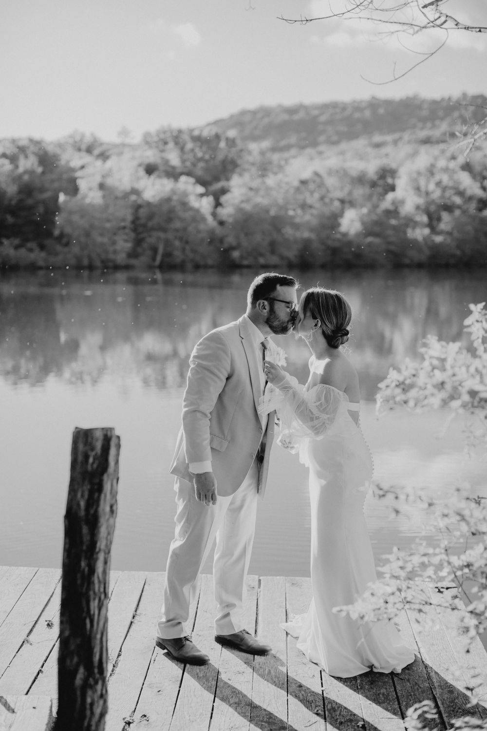 A romantic black and white photograph of a couple embracing on a wooden dock overlooking a serene lake. PA wedding Photographer