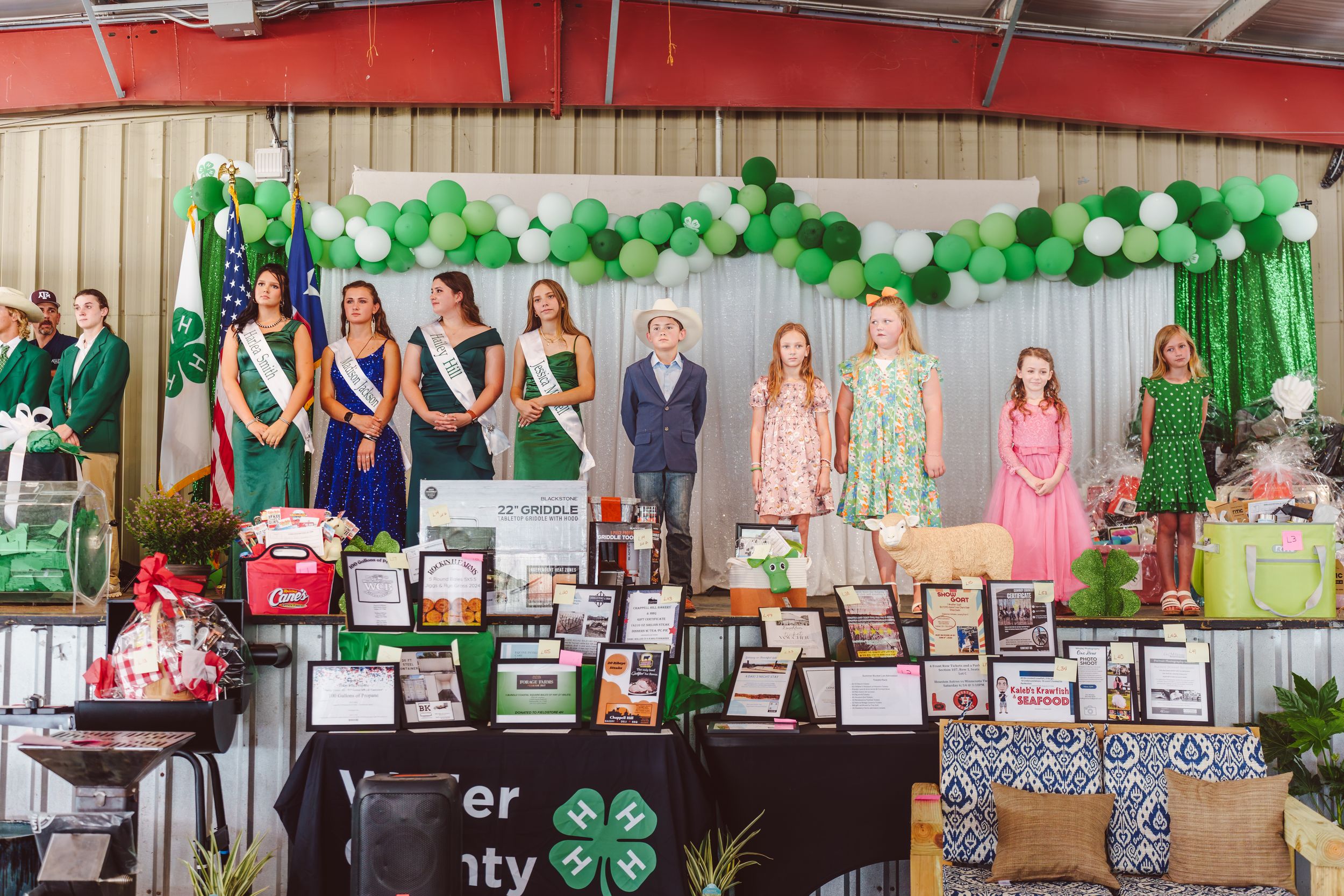 A 4-H youth club display with green decorations and award certificates showcases achievements at a community event.
