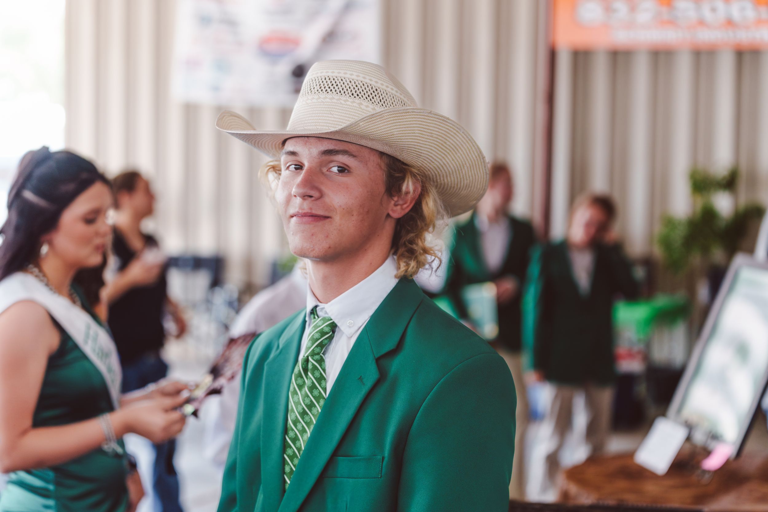 A person wearing a green blazer, cowboy hat and polka dot tie stands at an event.