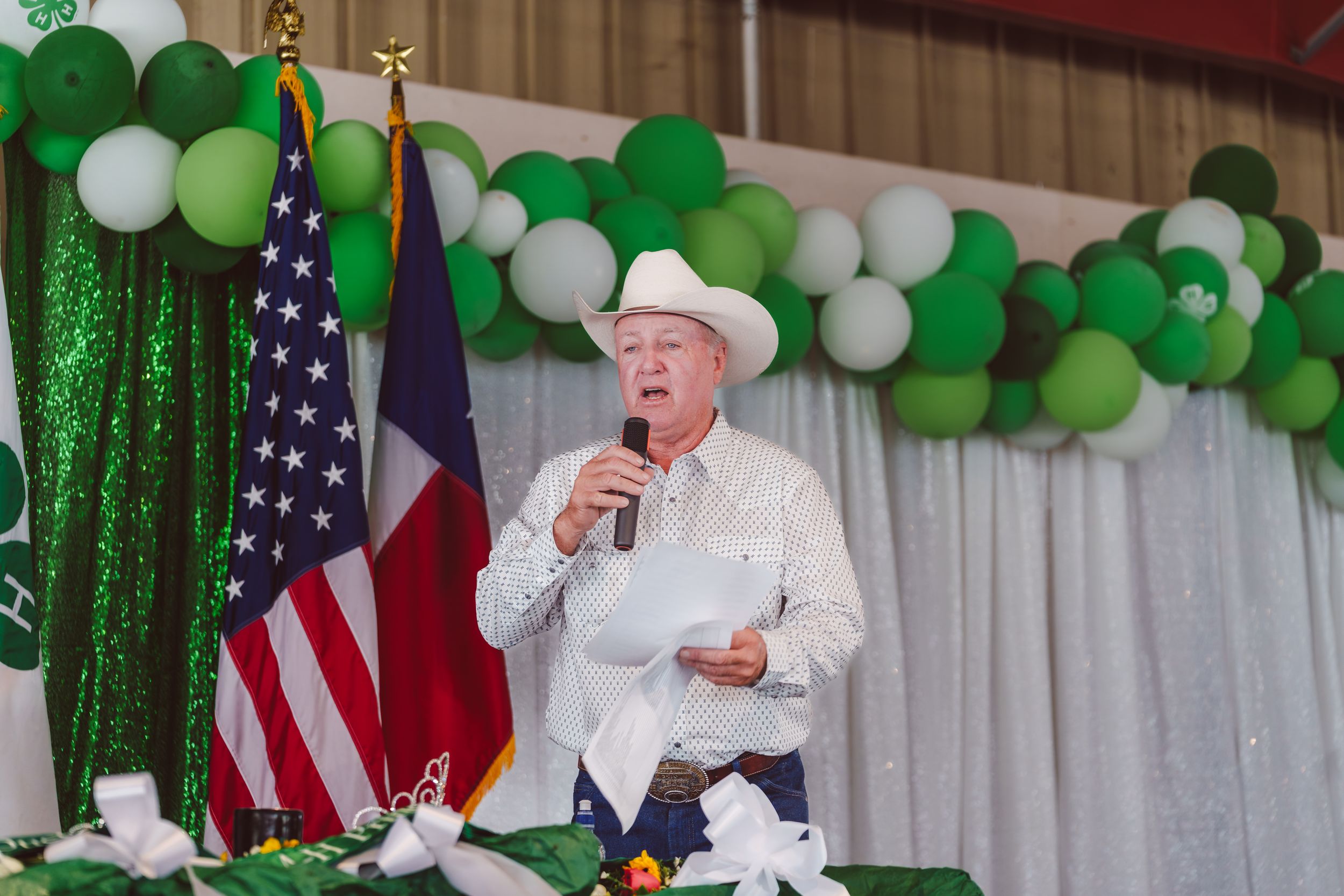 A festive St. Patrick's Day celebration with green and white balloons, American flags, and someone speaking at a podium.