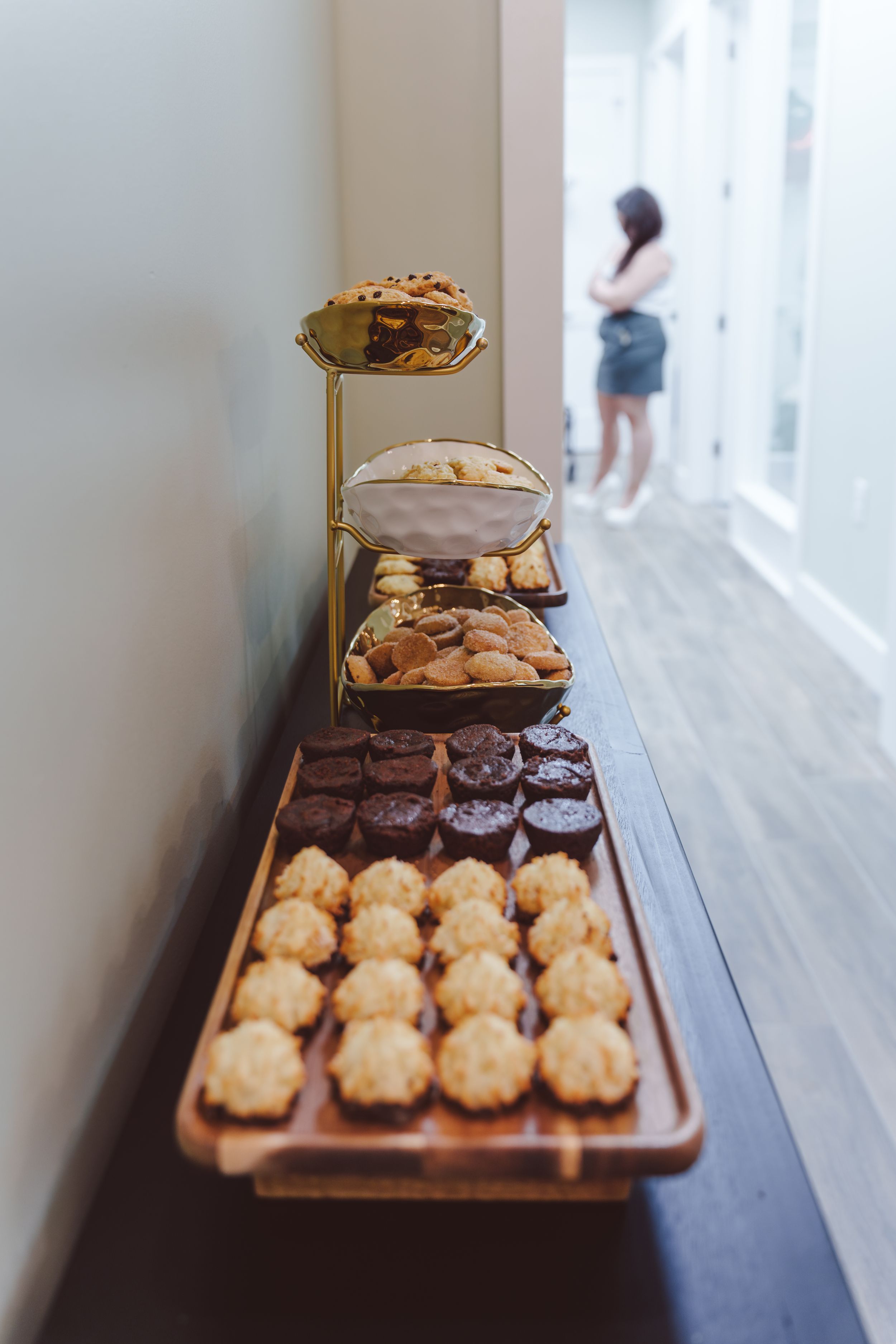 Wooden serving board displays freshly baked pastries and desserts arranged in rows on a dark surface near a window.
