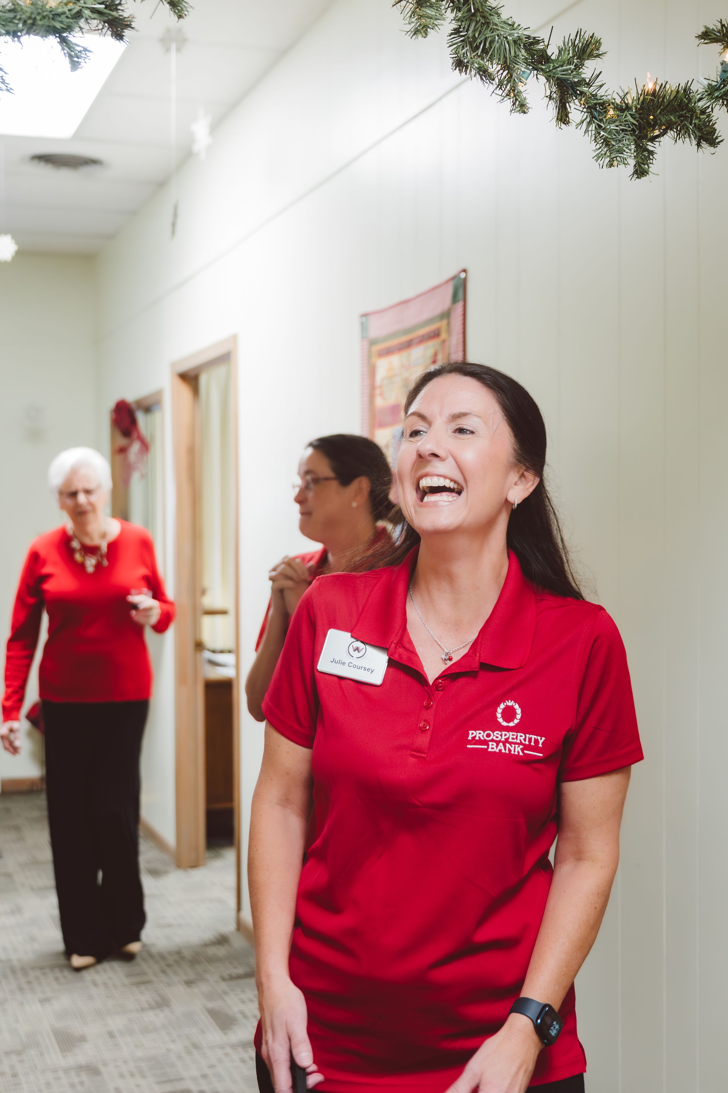Healthcare workers in red uniforms share a joyful moment in an office hallway decorated with holiday garland.