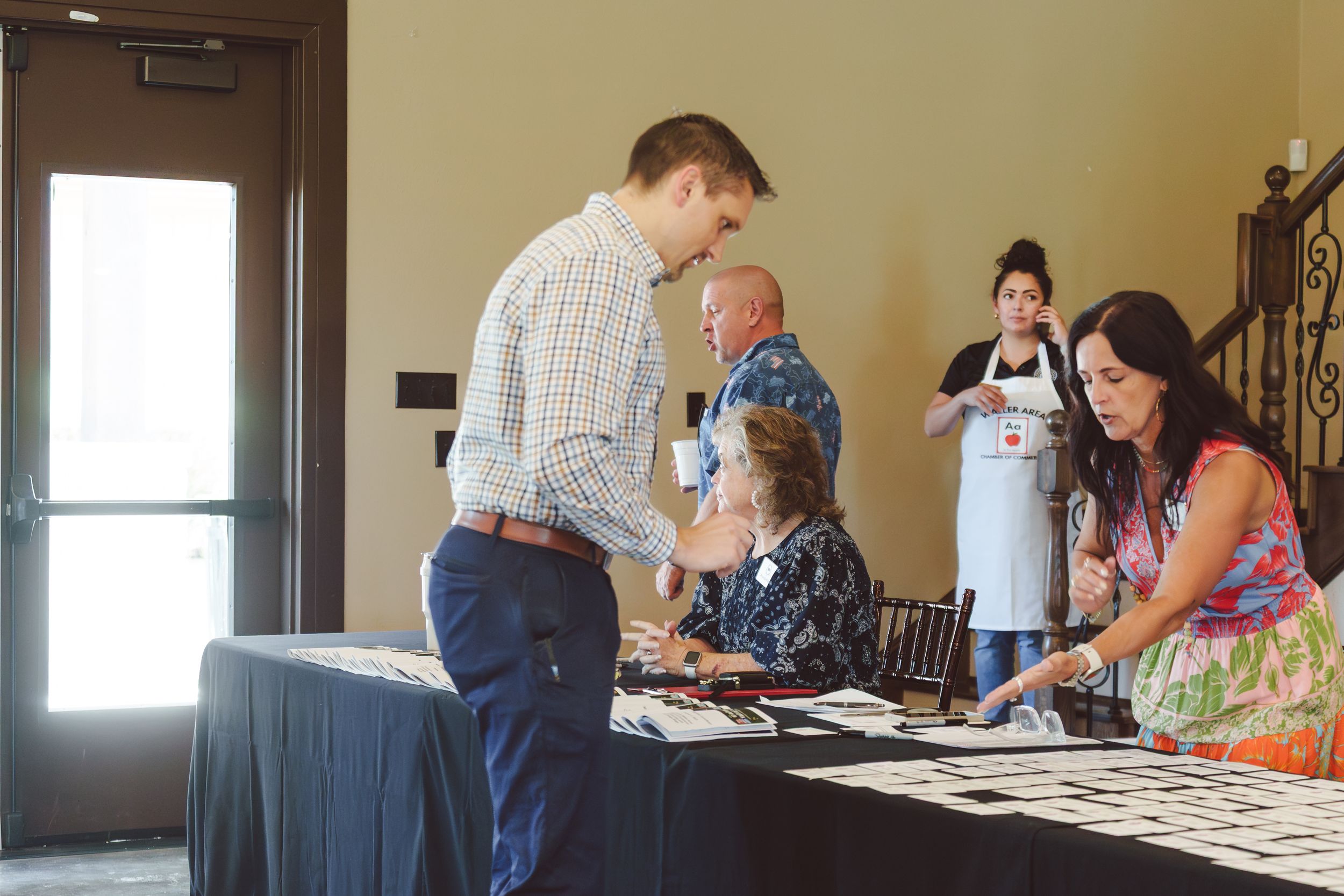 People gathered in a room looking at items displayed on tables during what appears to be an exhibition or event.