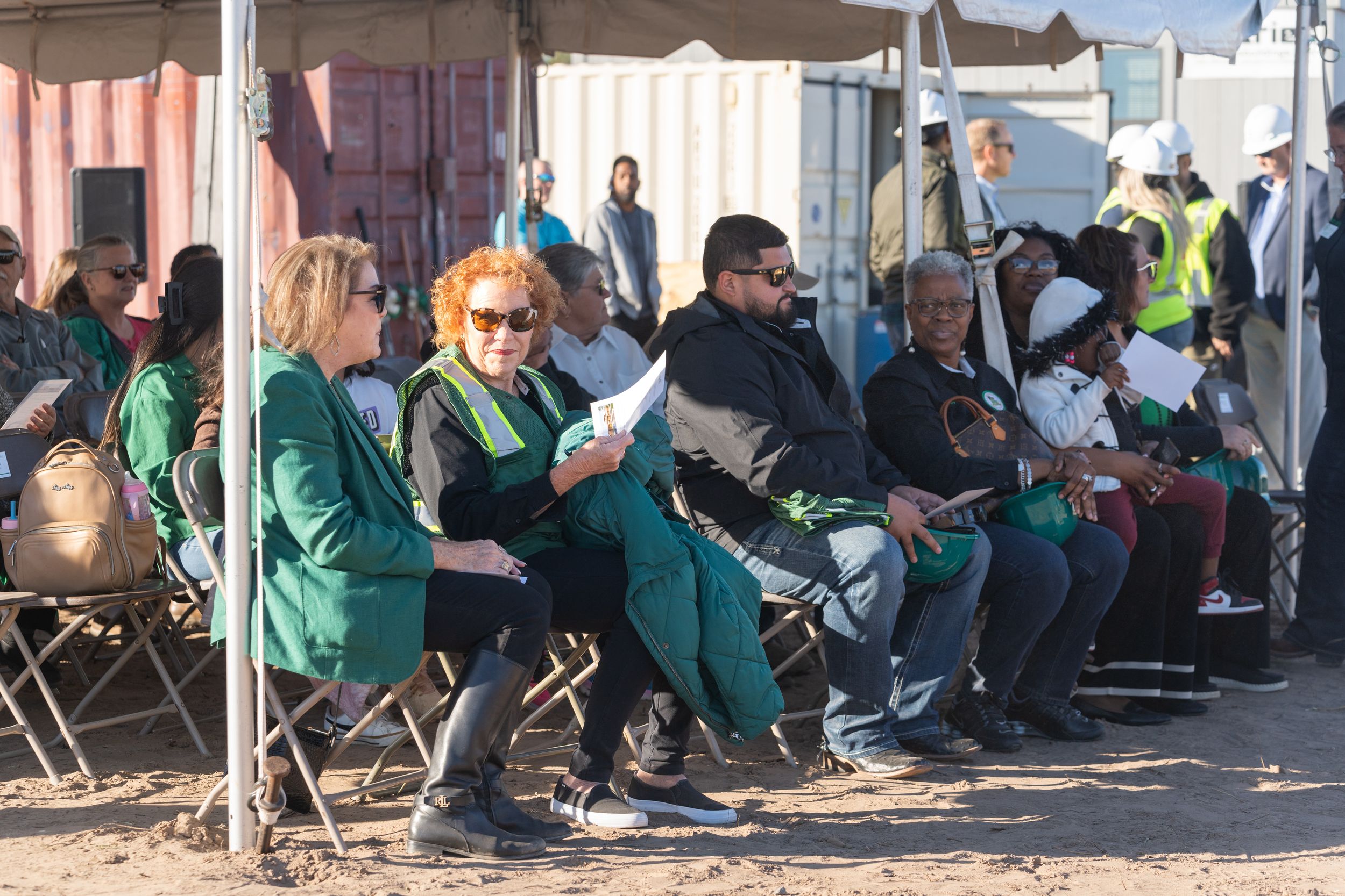 Panoramic view of people in green uniforms sitting in chairs lined up against a wall during an event.