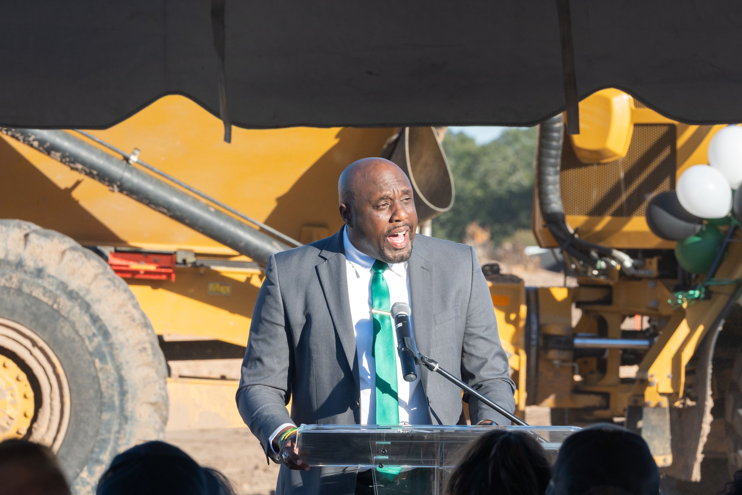 A yellow construction excavator machine is working at a job site with other equipment visible in the background.