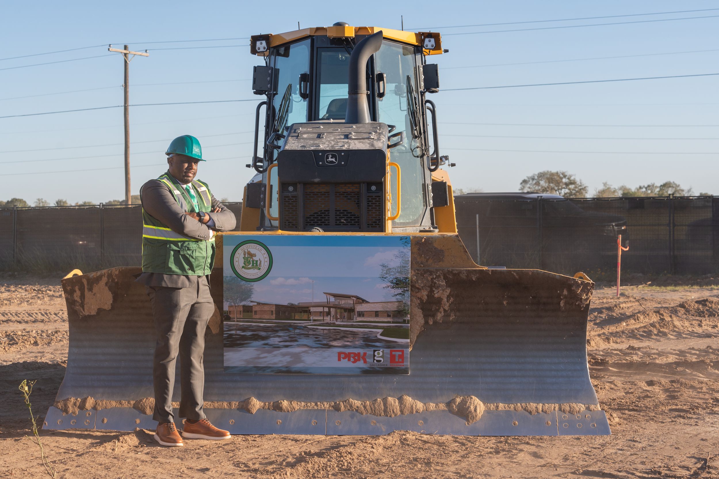 Construction worker stands beside a large yellow bulldozer at a dusty worksite during daytime.