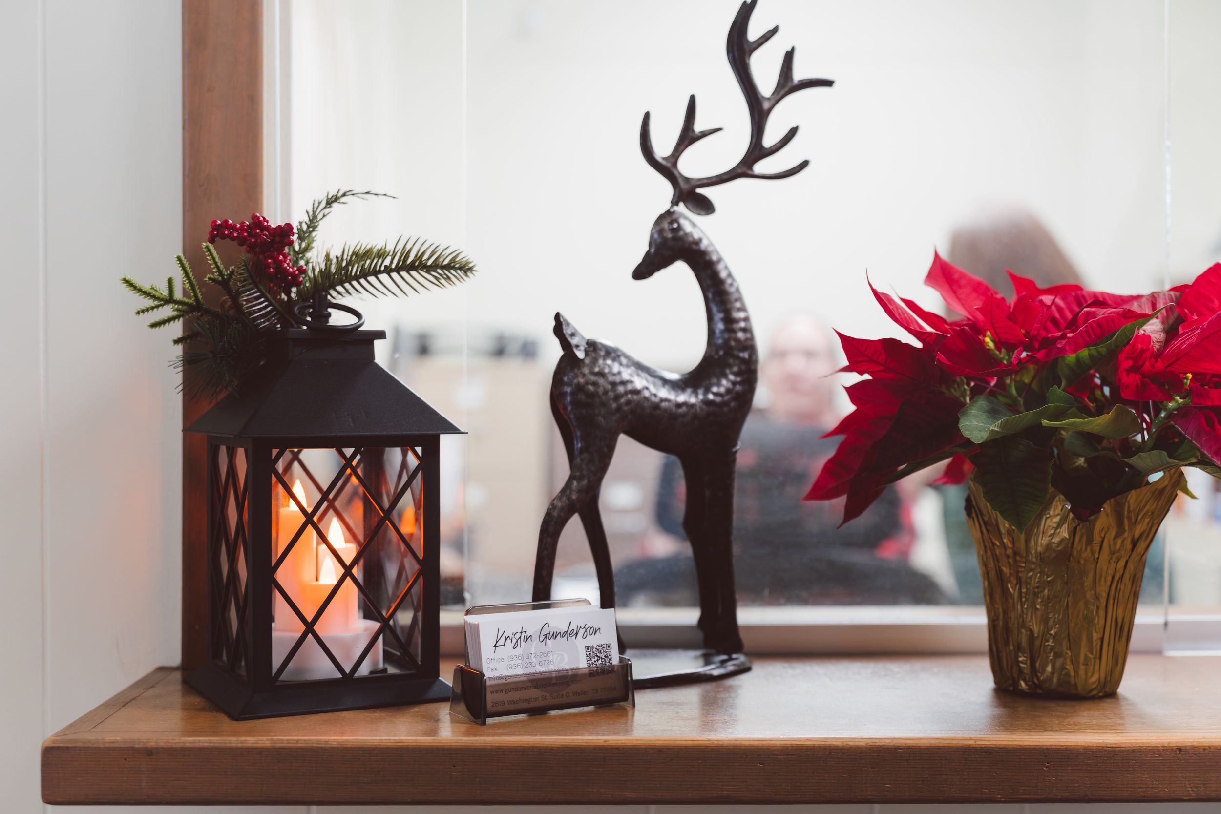 Holiday decor display featuring a black lantern with glowing candle, metal reindeer statue, and red poinsettia plant.