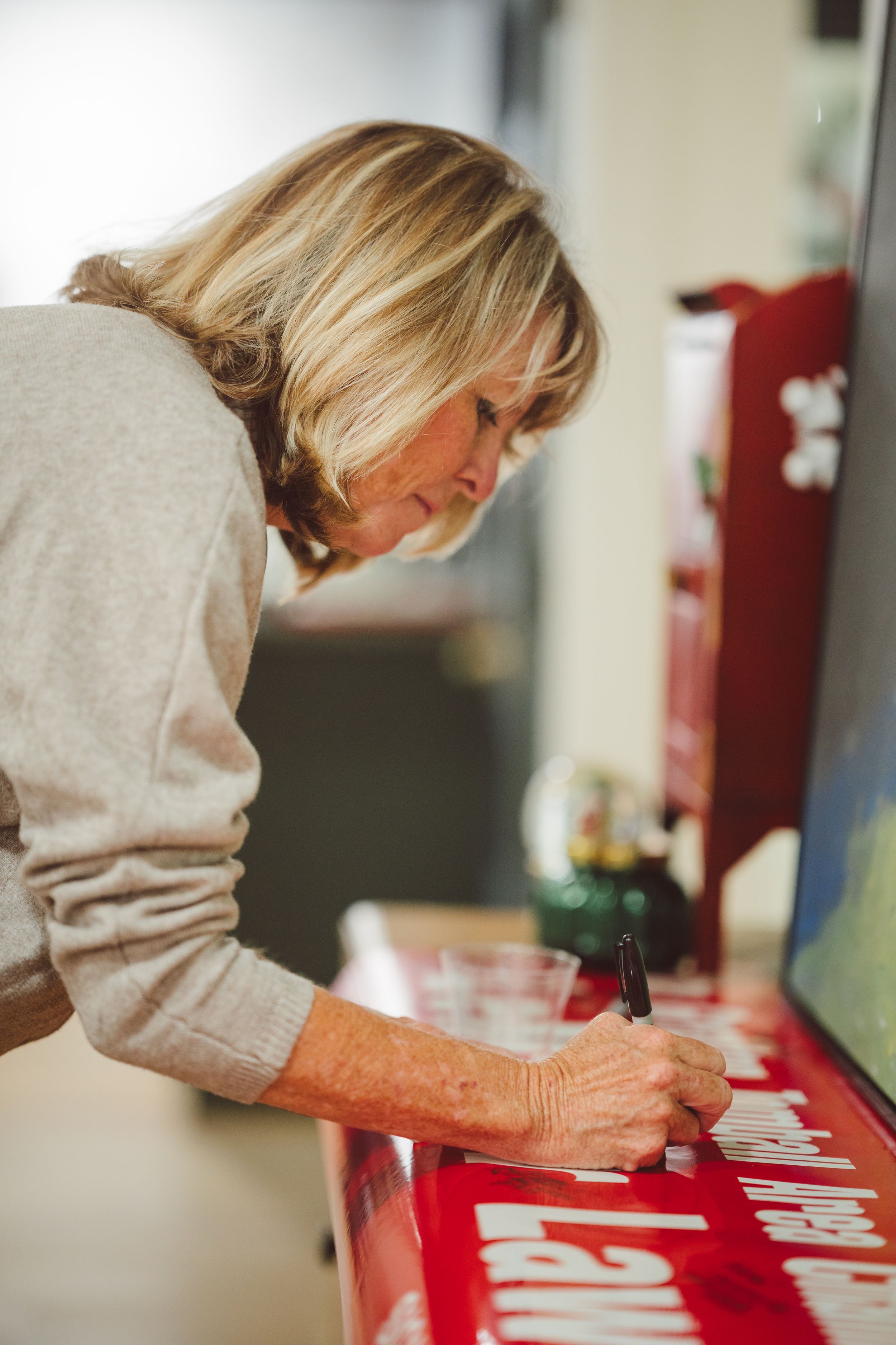 Person in beige sweater carefully signing or writing on red surface in sequence of progressive shots.