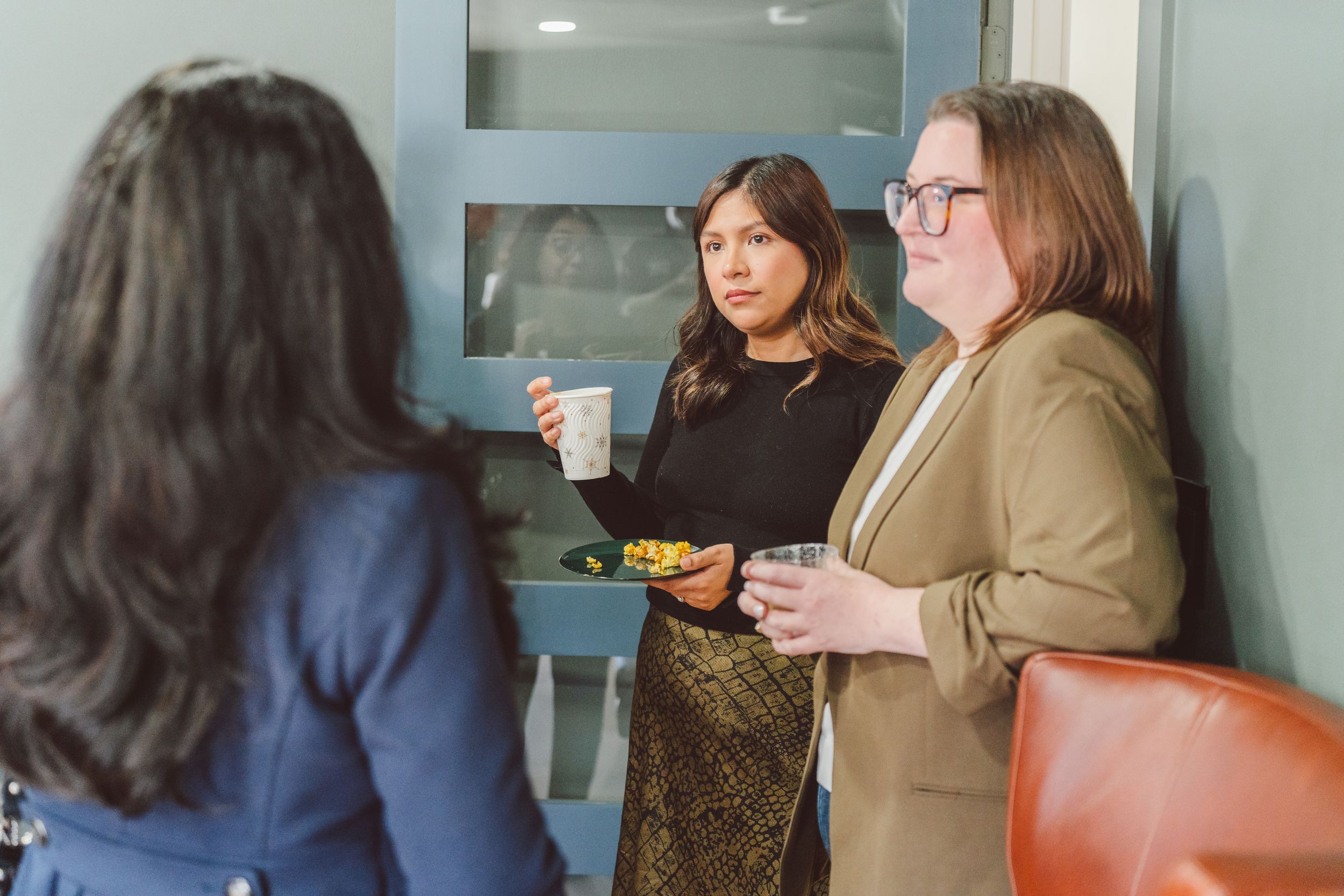A group of colleagues gather around a table during a casual office meeting while drinking coffee and having discussions.