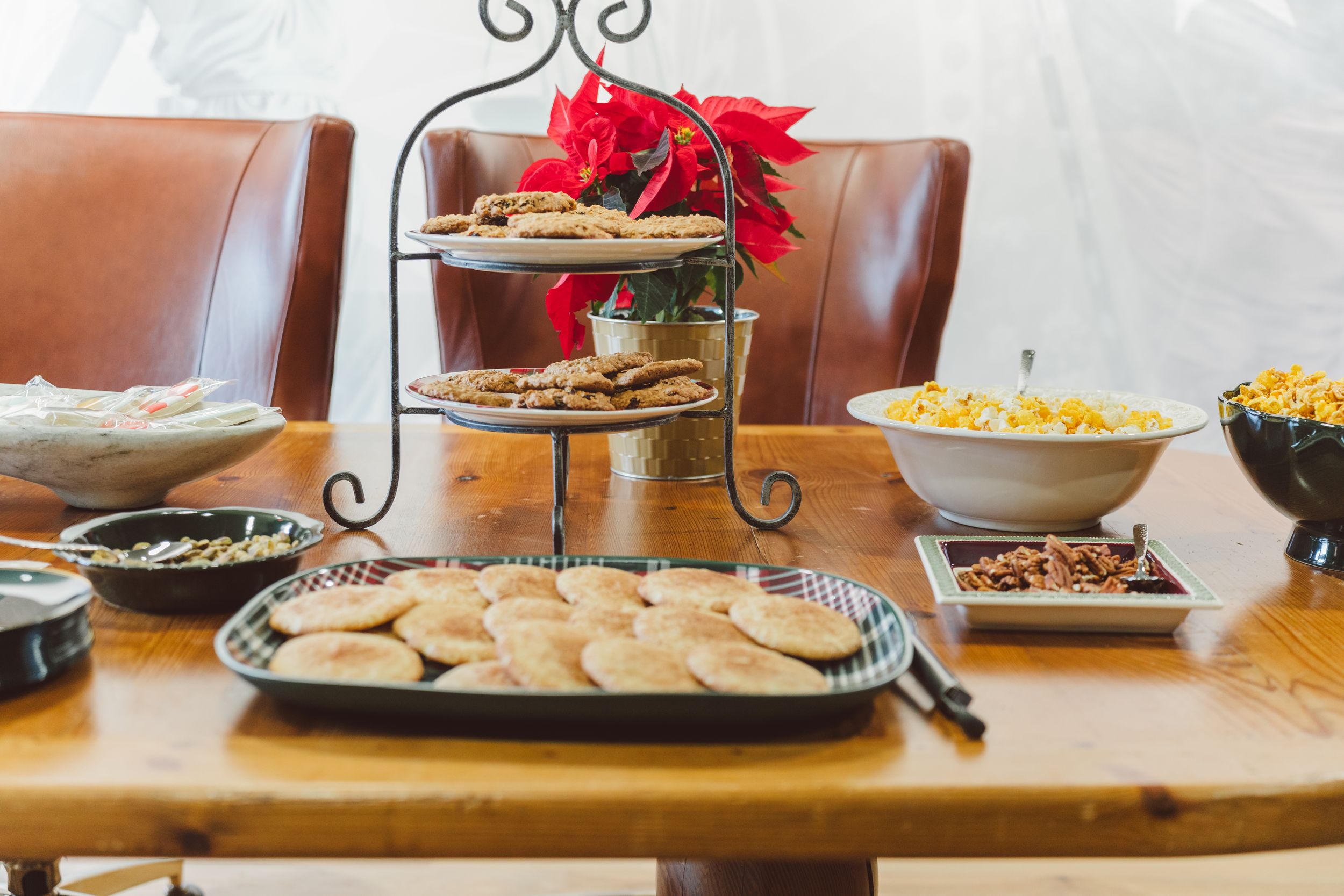 A wooden table set with various appetizers, snacks and dips for entertaining with red poinsettia flowers as decoration.
