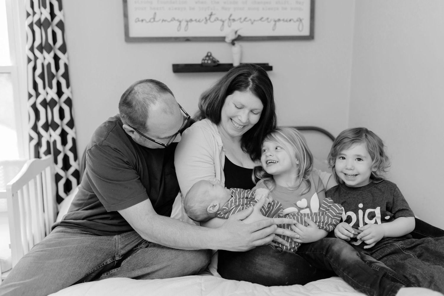 family seated together on bed holding newborn baby