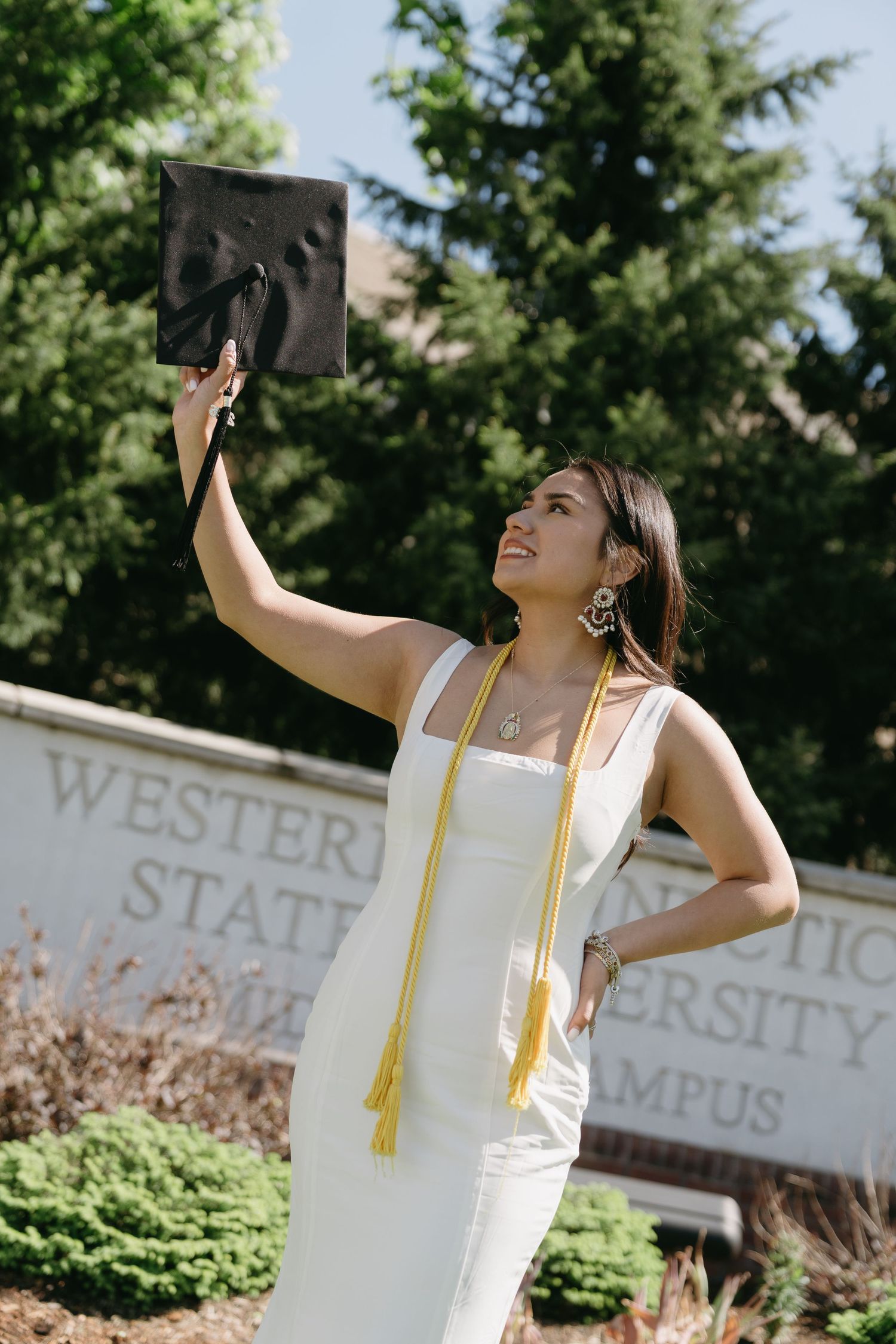 Joyful bride in flowing white dress holds fabric against bright blue sky.