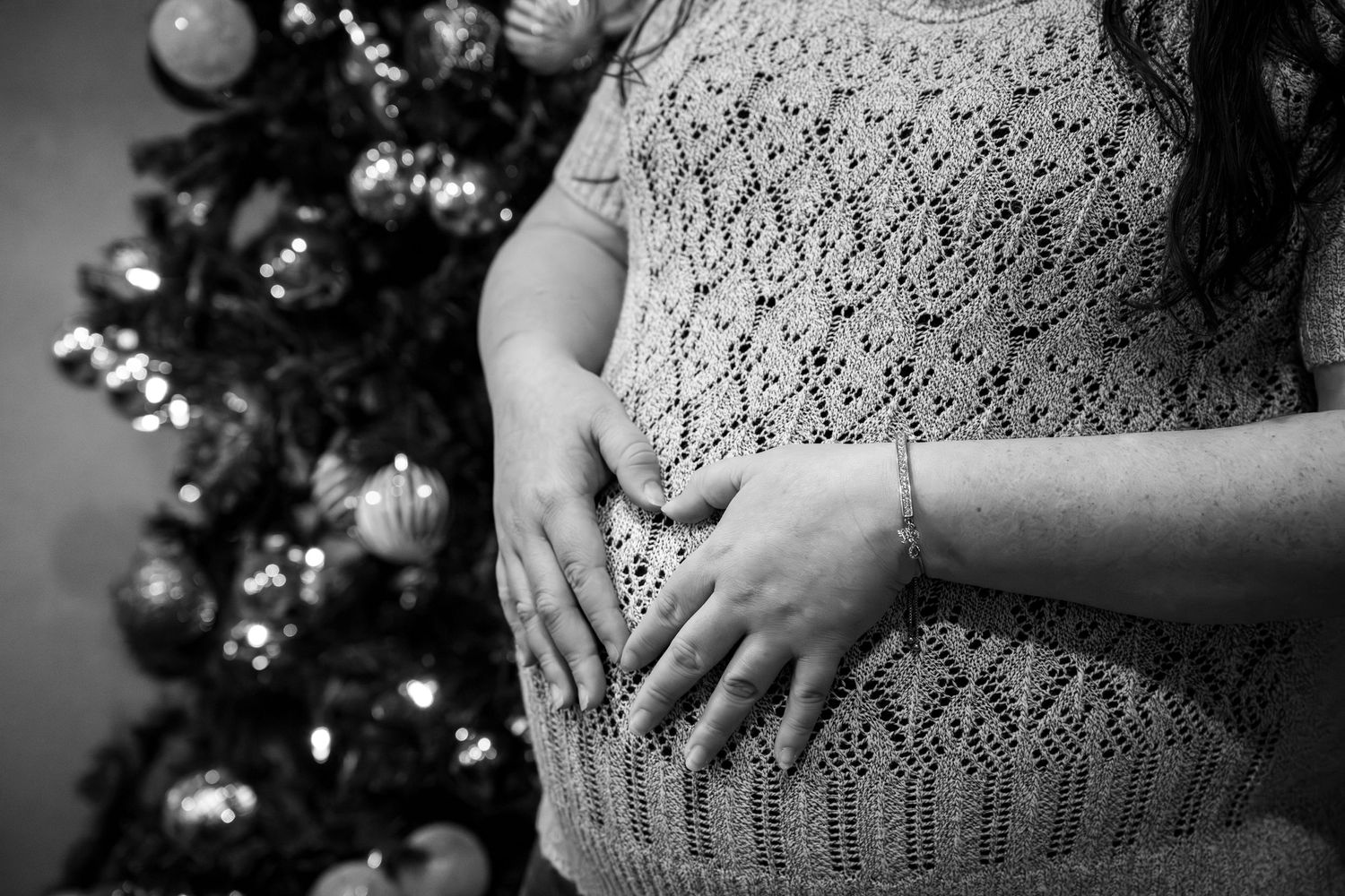 Black and white image of hands resting on a knit sweater with a Christmas tree in the background.