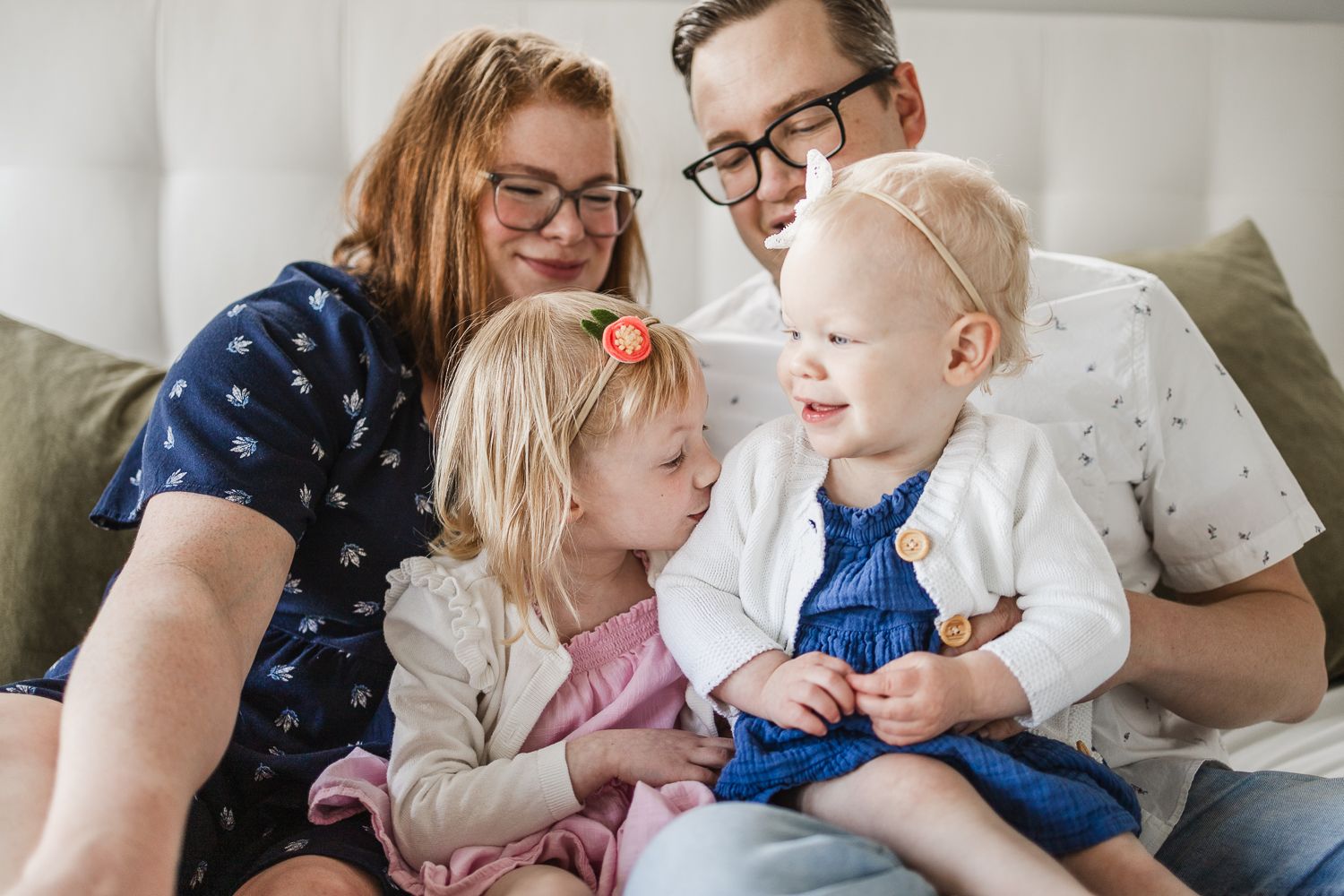 Two children sit on their parents' laps as the older chid kisses her sister's arm