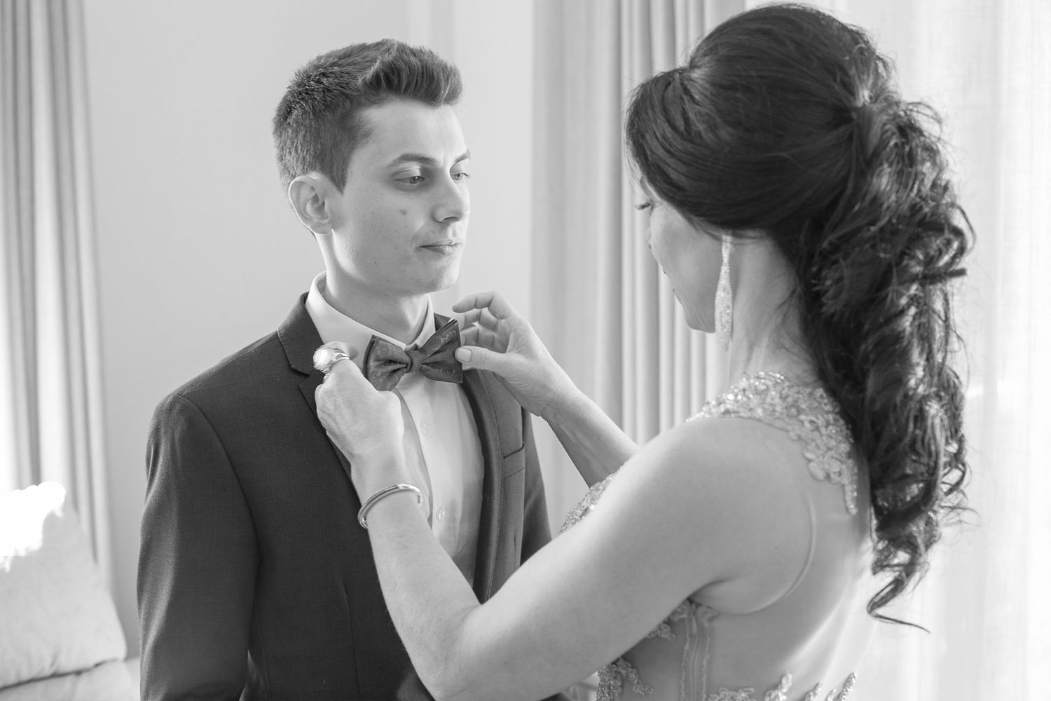 A bride adjusts the groom's bow tie in an intimate black and white wedding moment.