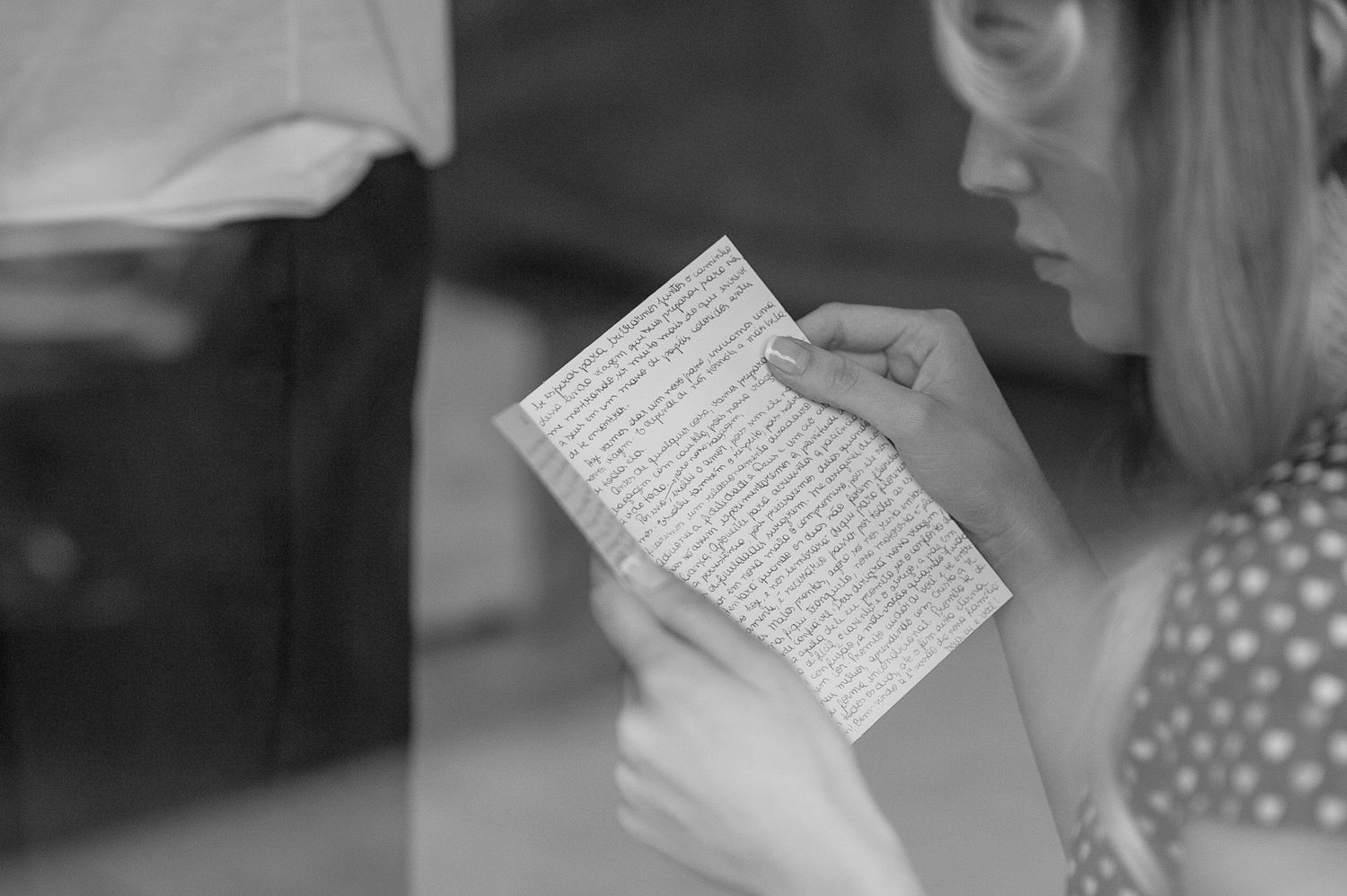 A woman in polka dot dress reads from a paper in black and white photography.
