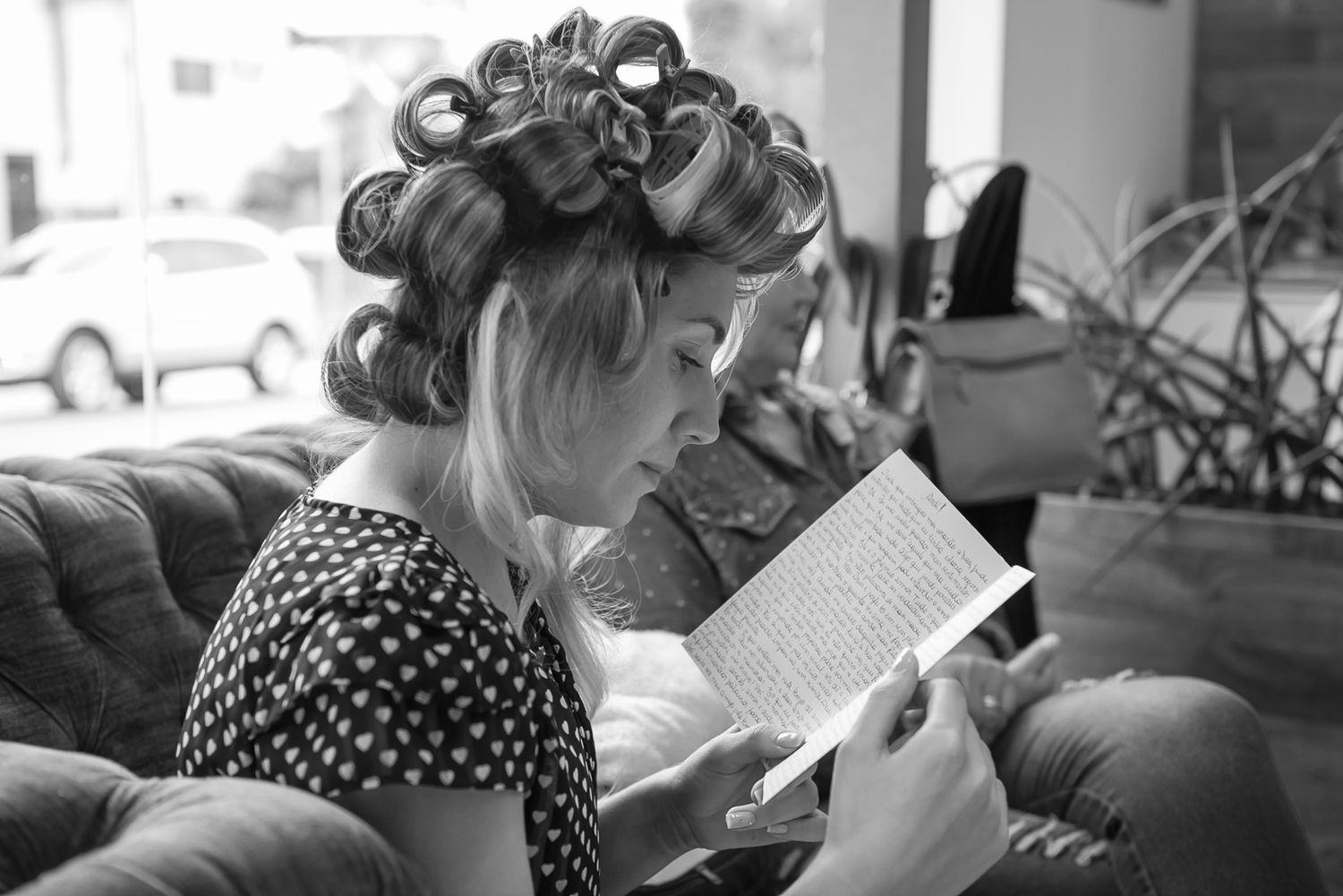 Woman with hair in curlers reads a book while seated on a sofa in retro styling.
