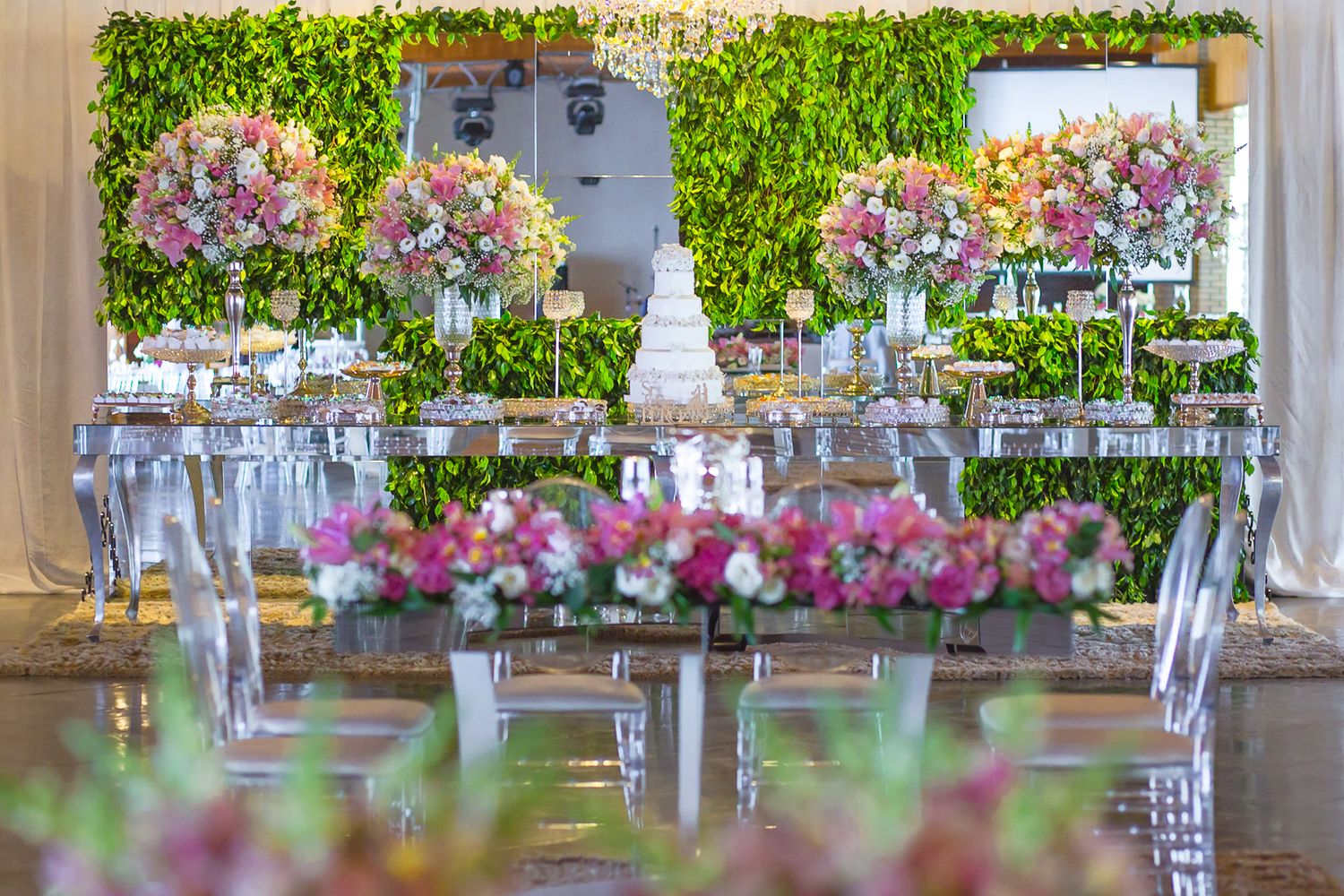 Luxurious wedding reception decor featuring pink floral arrangements and green wall backdrop.