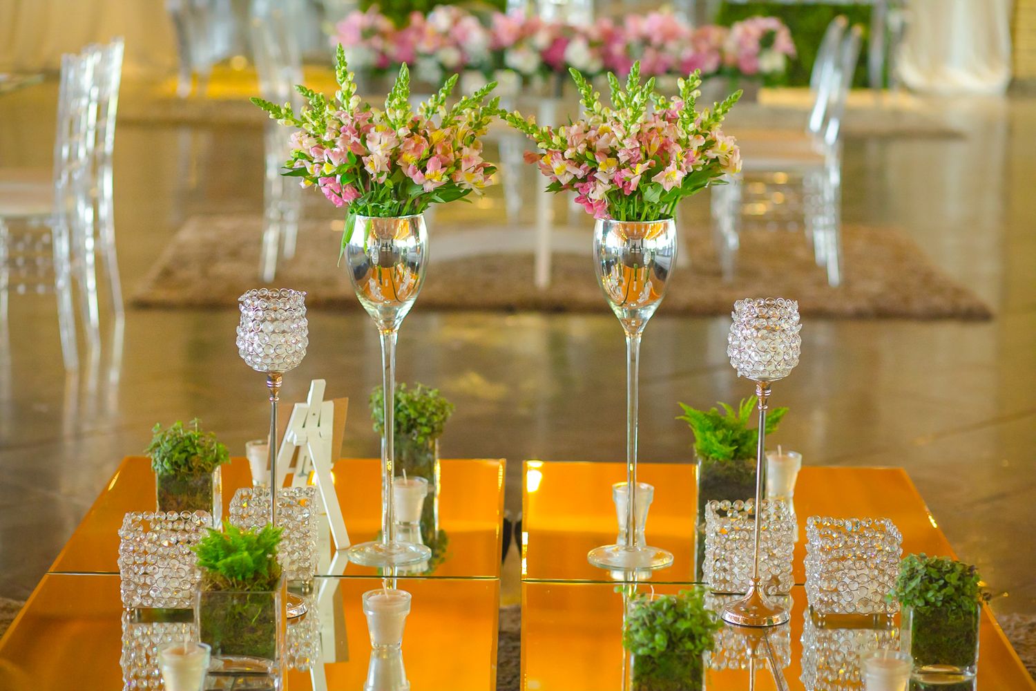 Crystal glassware and delicate floral arrangements on gold-toned tables at an elegant event.
