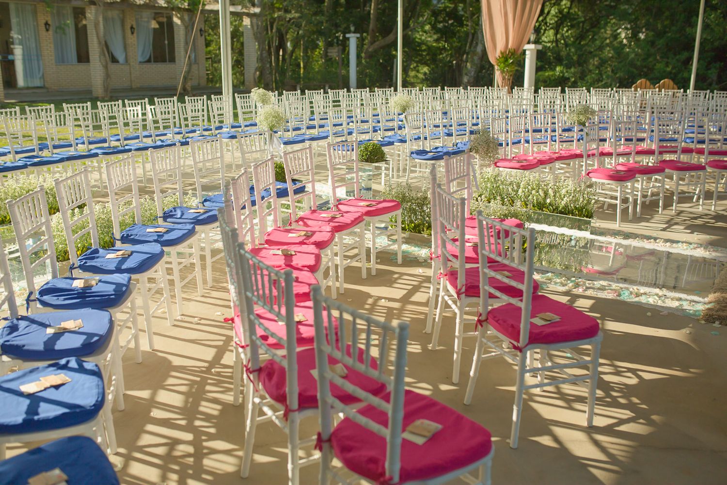 Outdoor wedding ceremony setup with blue and pink cushioned chiavari chairs in curved rows.