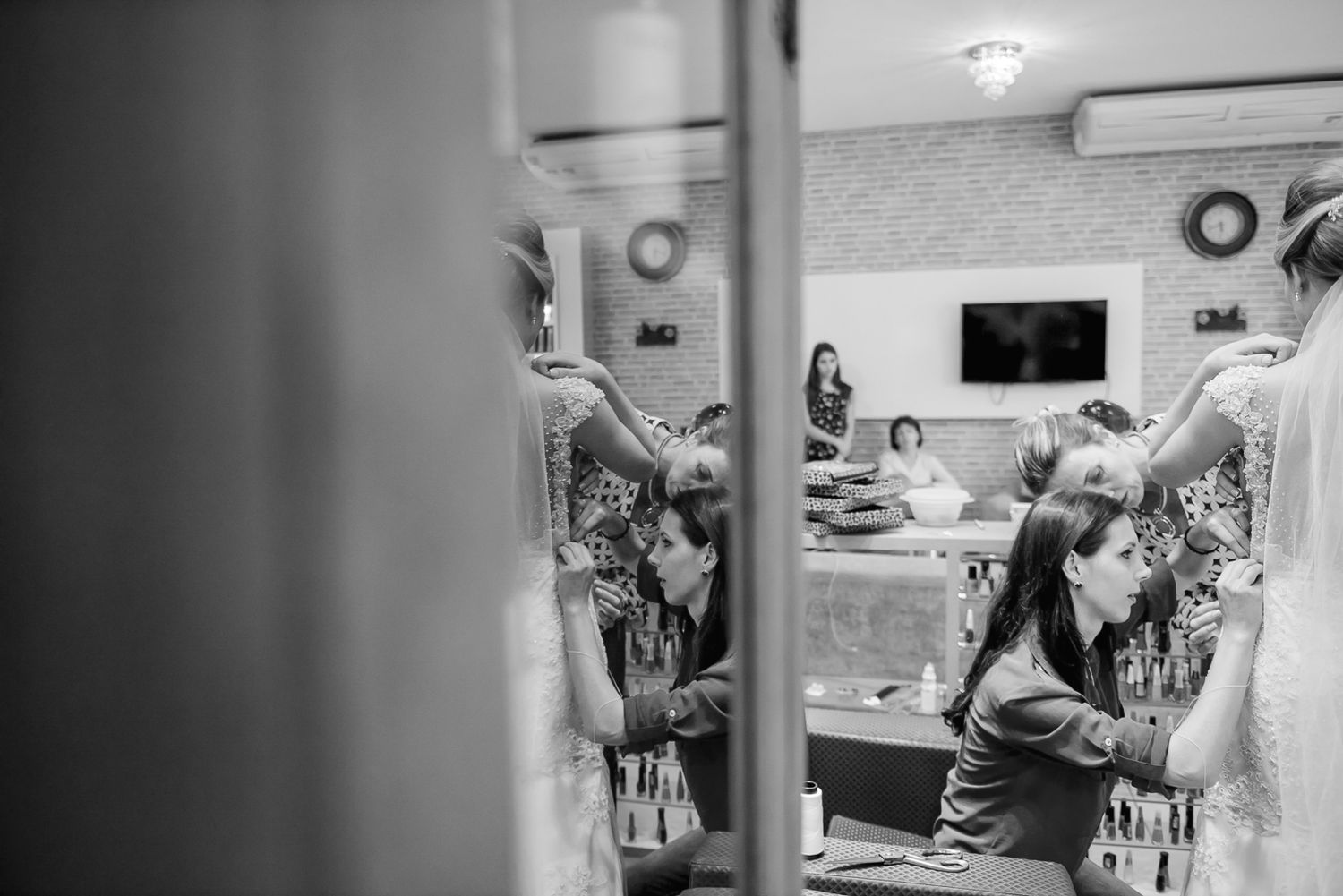 Behind-the-scenes view of a bridal fitting appointment through a doorway in black and white.