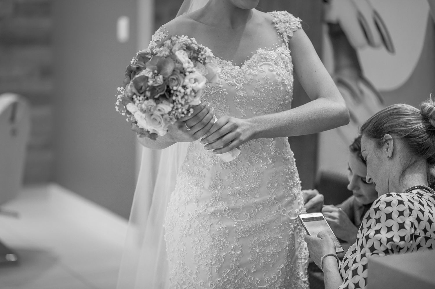 Close-up of lace wedding dress details and bouquet during final fitting.