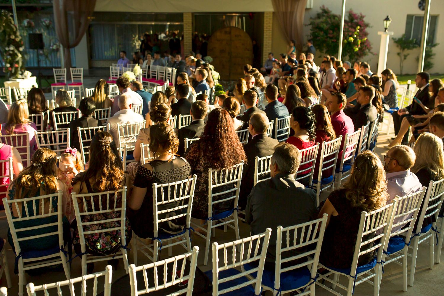 Wedding guests seated in white chairs at an outdoor reception venue.