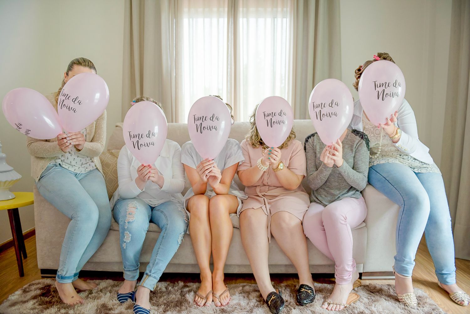Fun bridal party photo with pink balloons covering faces while sitting on couch.
