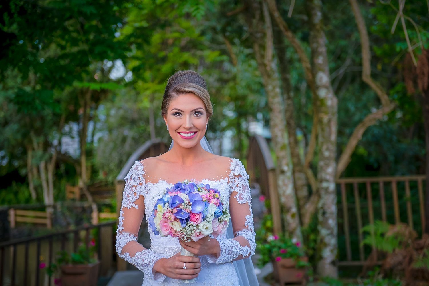 A bride holds a vibrant purple and blue floral bouquet while posing outdoors on a garden path.