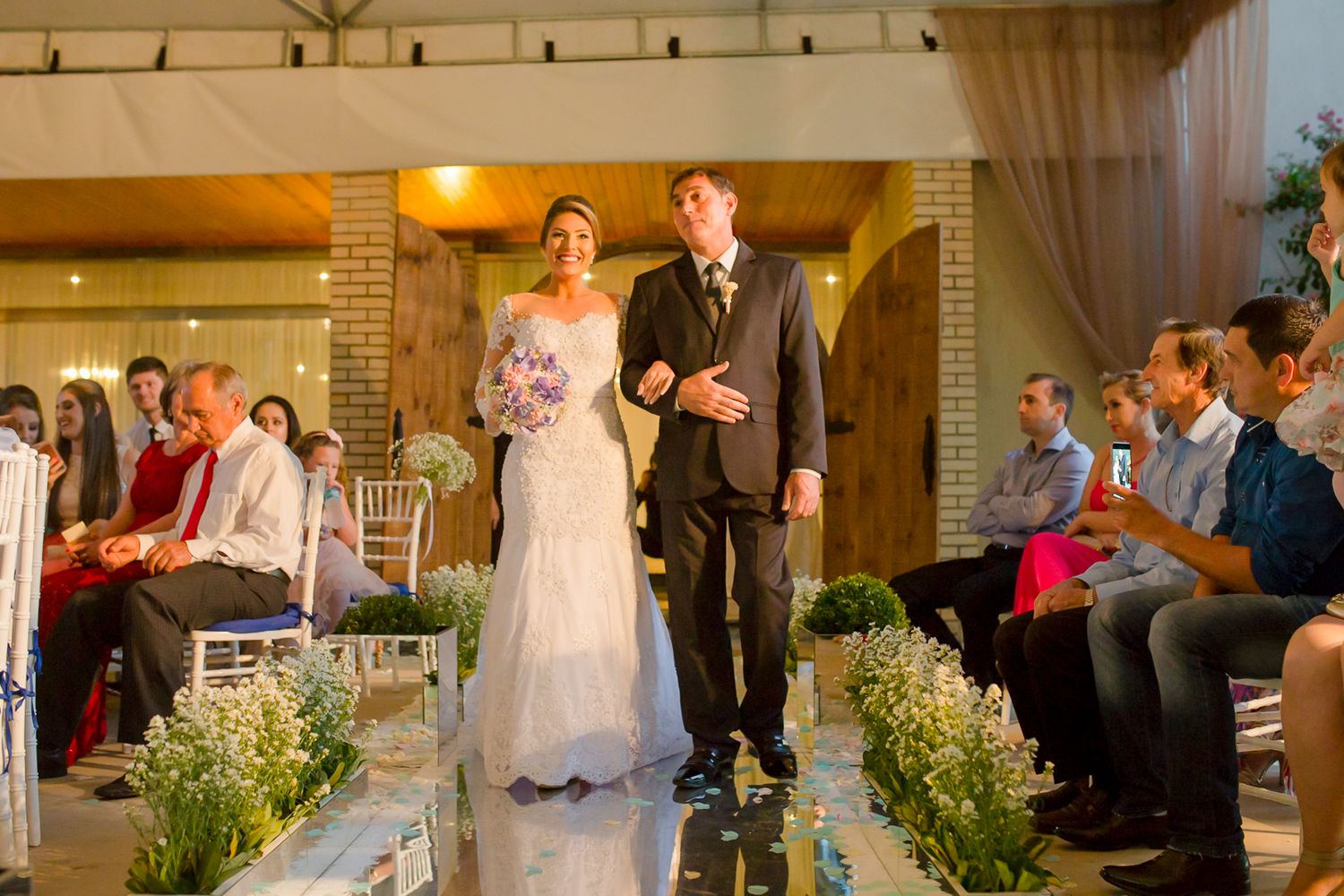 Wedding ceremony in an elegant indoor venue with floral aisle decorations and seated guests.