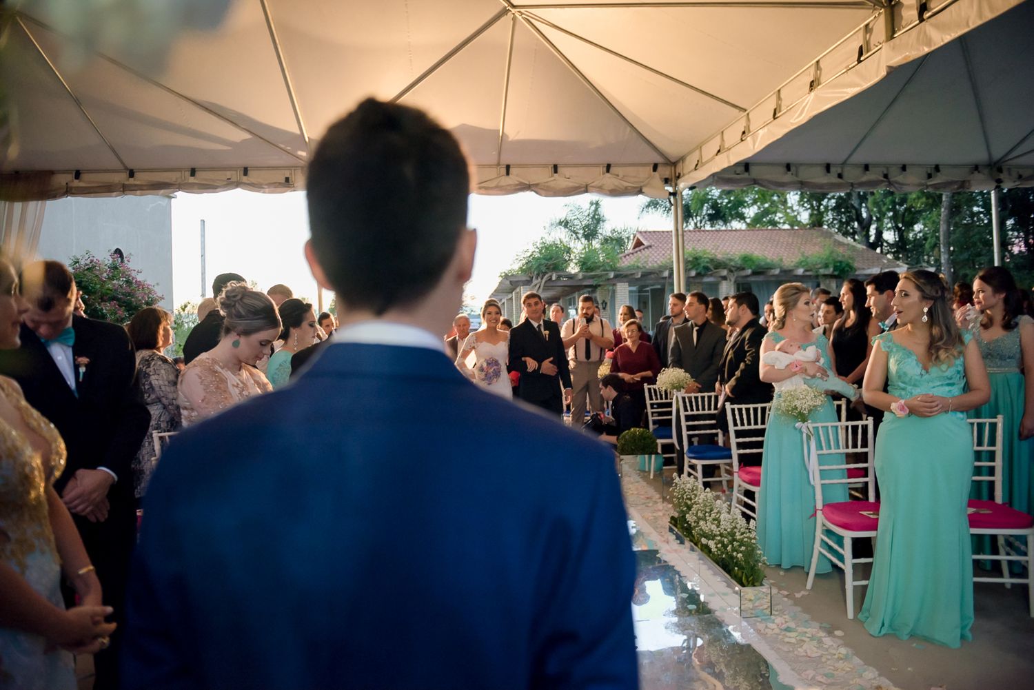 Wedding guests seated under white tent canopy during outdoor ceremony.